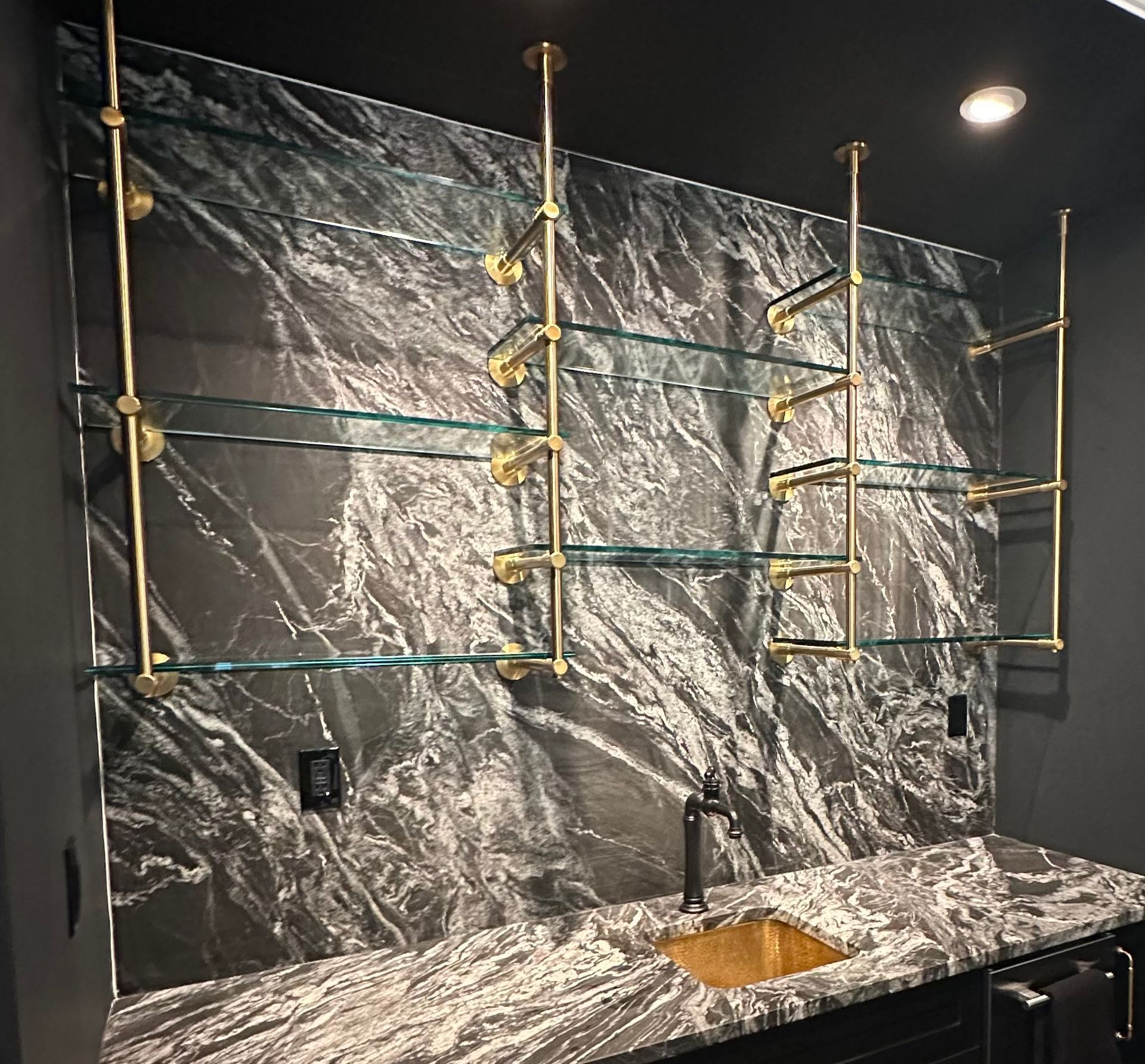 Bathroom vanity with marbled tile wall, brass rod shelving, and a stone countertop sink