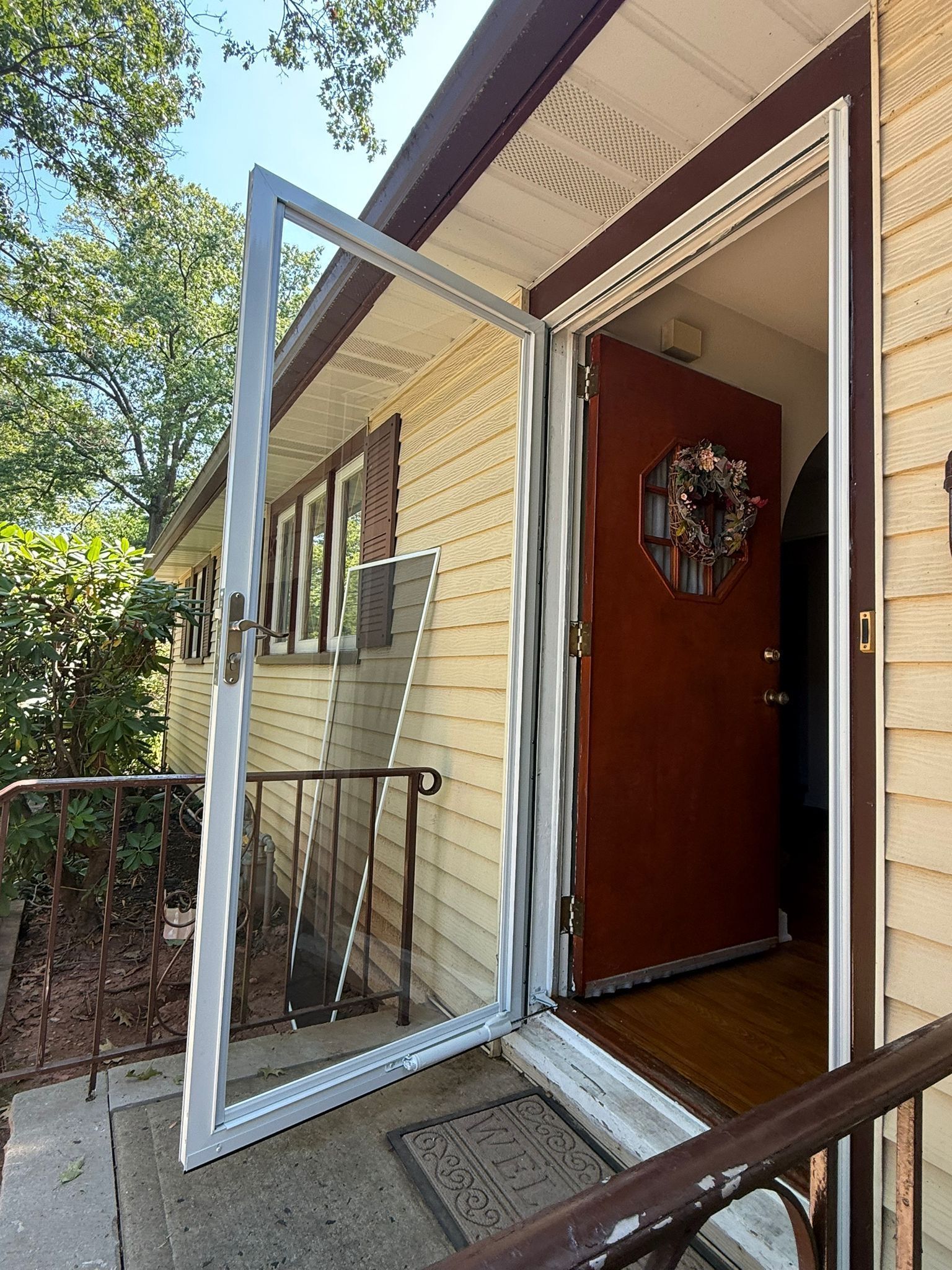 Open front door with screen door ajar, revealing a wreath on the inside door and an outdoor porch railing.