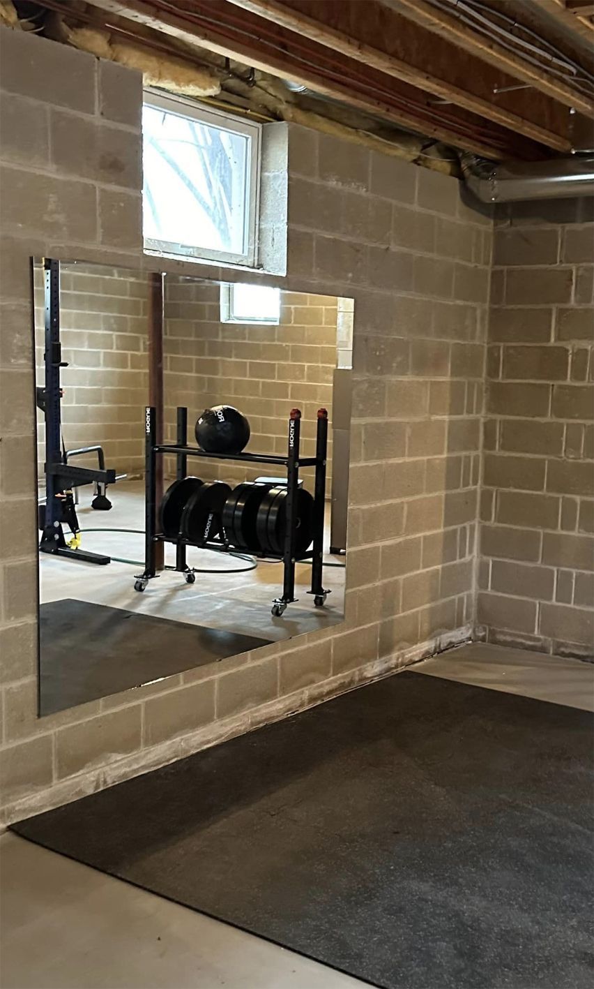Basement workout area with a wall mirror, bench, and black exercise equipment on a dark mat.