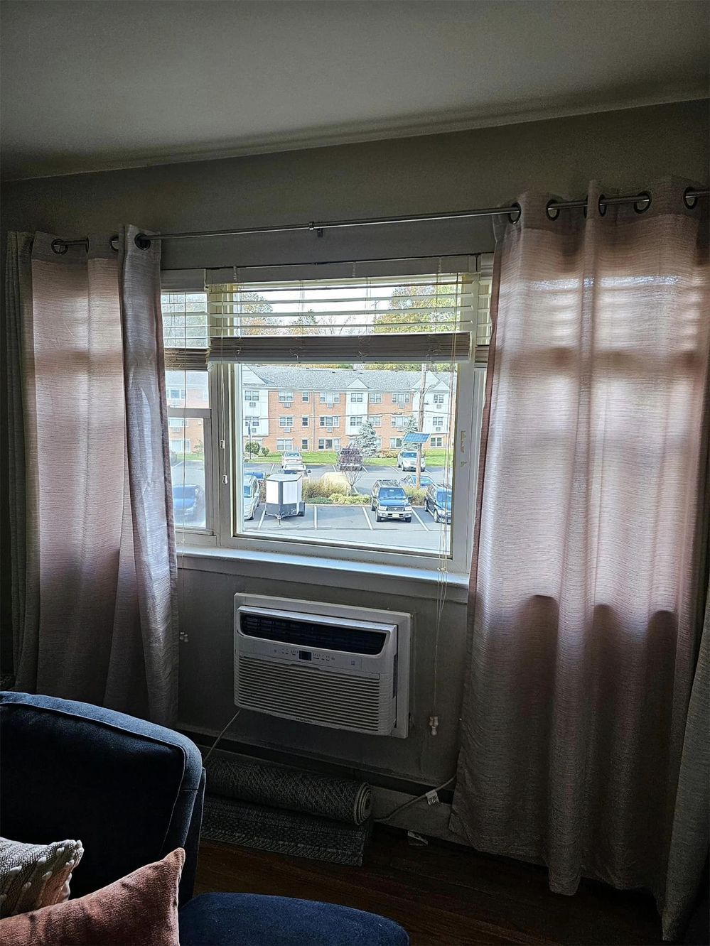 Living room window with sheer curtains, an air conditioner, and a view of apartment buildings outside.