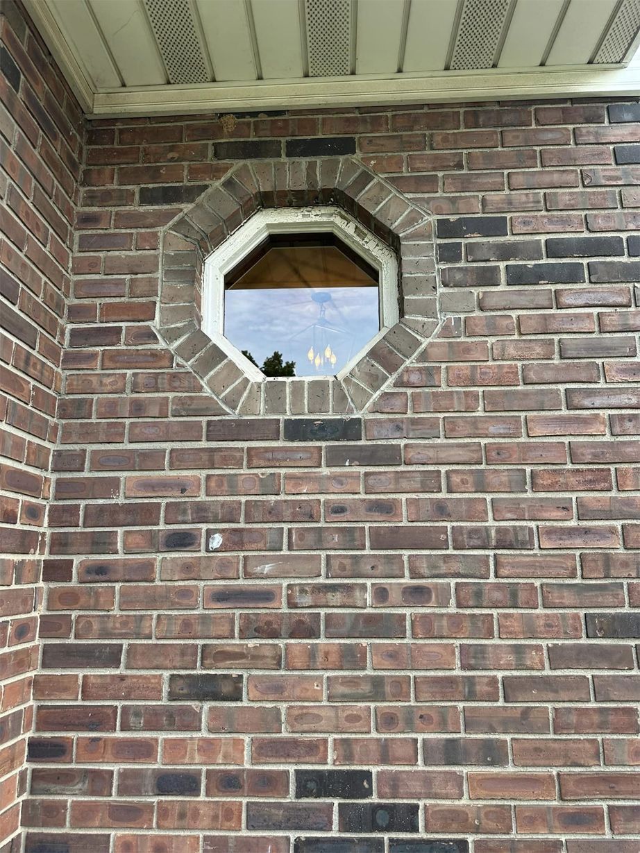 Octagonal window in a red brick wall with white trim and sky visible through it