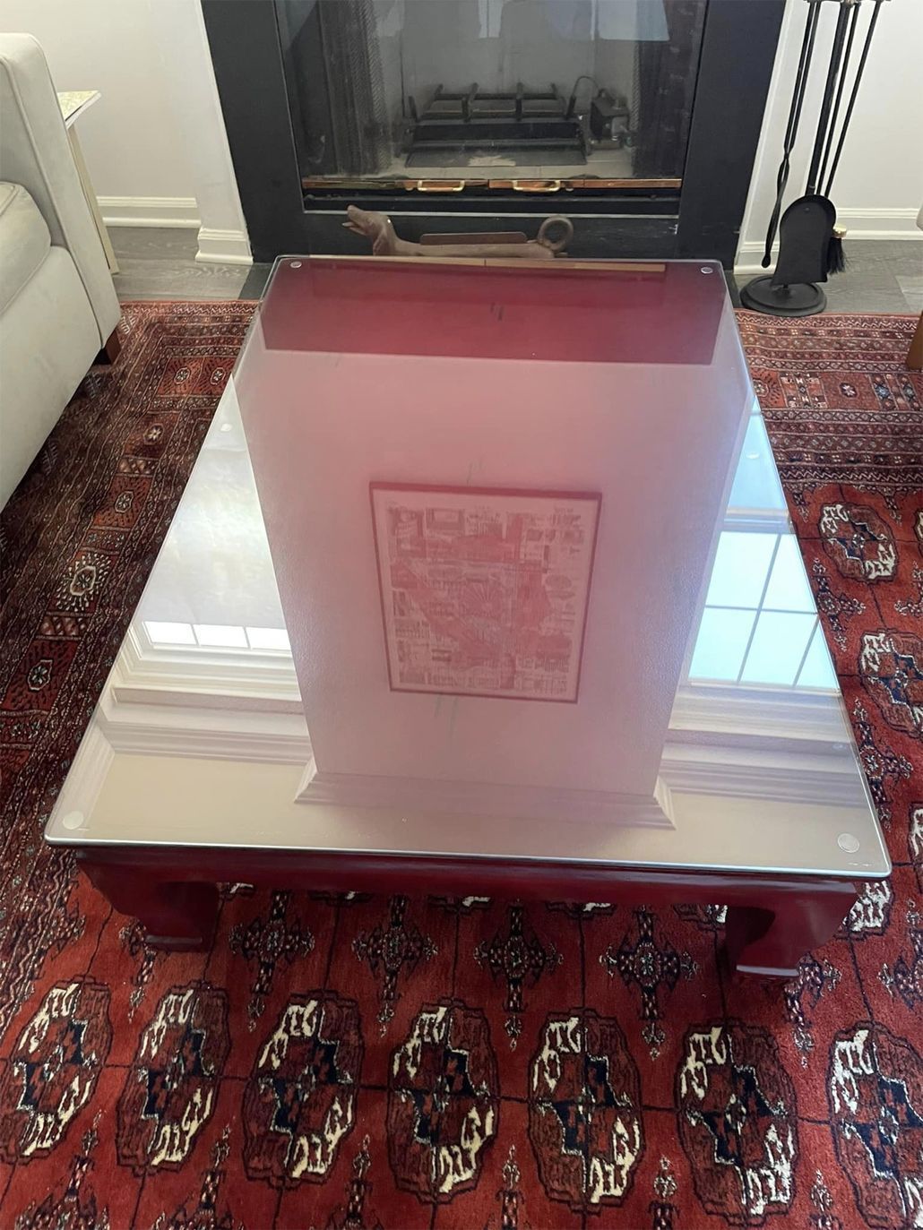 Glass coffee table on a red patterned rug in front of a fireplace.