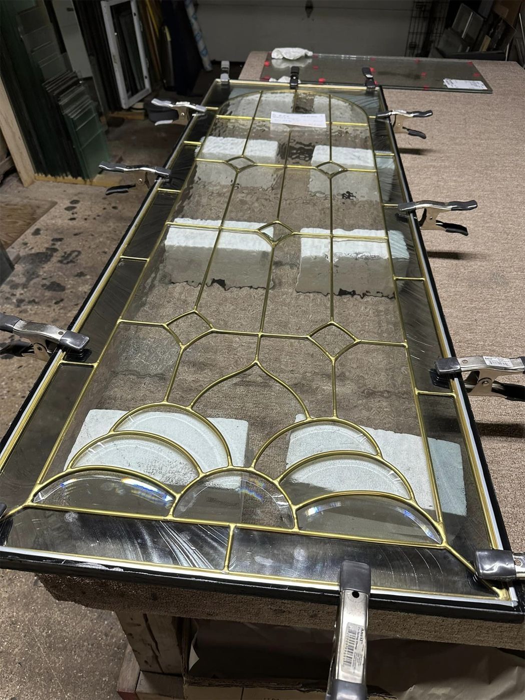Stained glass window panel on a workbench, with yellow lead lines and white glass sections.