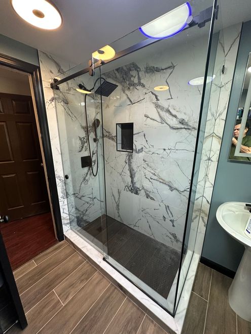 Modern bathroom with a glass shower enclosure, marble-pattern tile, and wood-look flooring