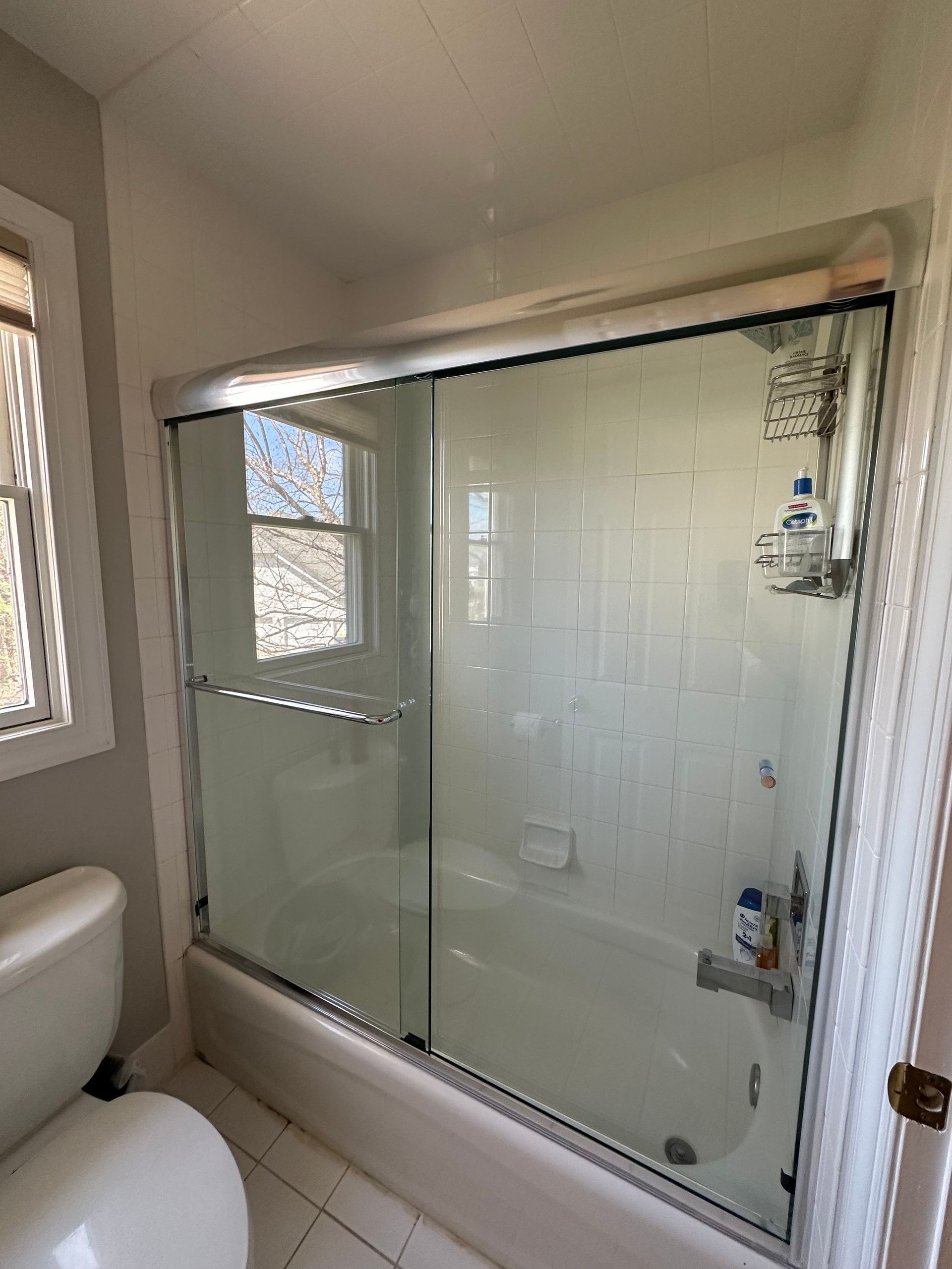Bathroom with glass-enclosed shower, white tile walls, and a window beside the tub.