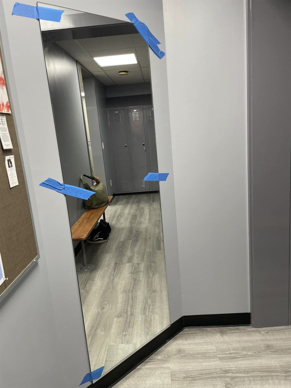 Tilted hallway mirror taped with blue painter’s tape in a gray corridor