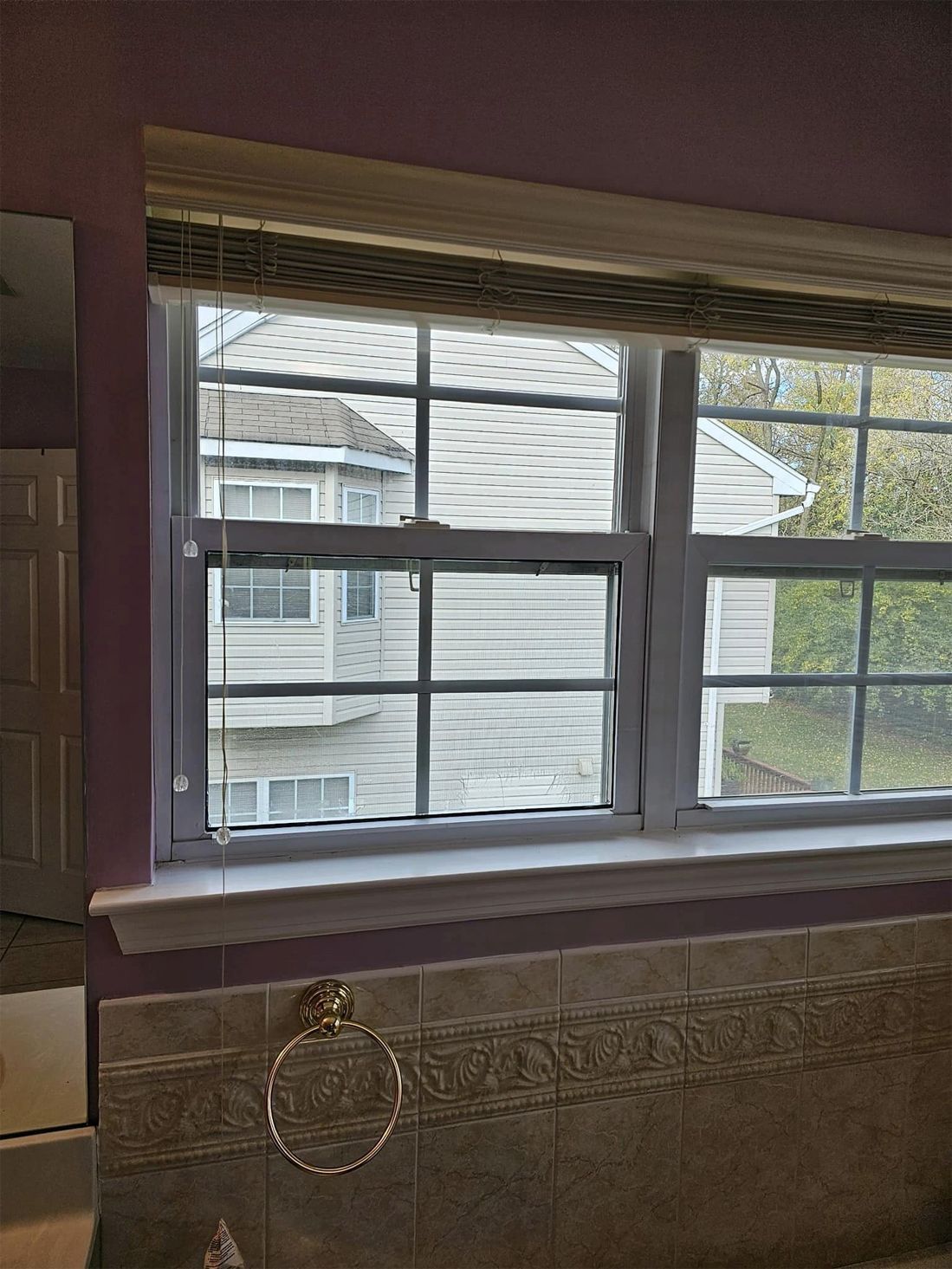 Interior window with white blinds, purple wall, and a view of neighboring houses outside