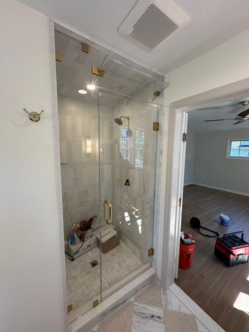 Glass shower stall under construction in a bathroom, with a red toolbox visible in the adjacent room.