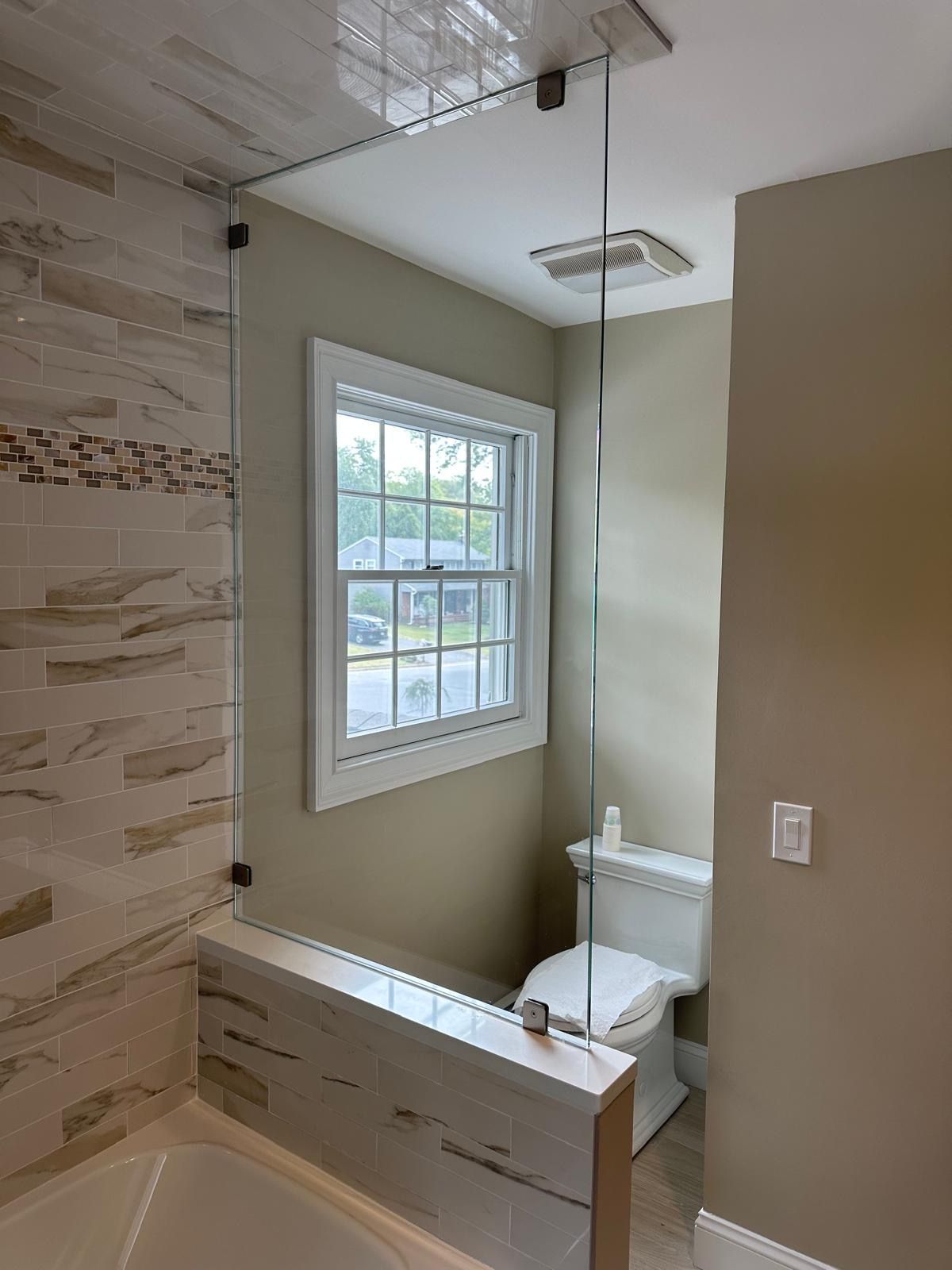Small bathroom with glass shower, white window, and beige tile walls.