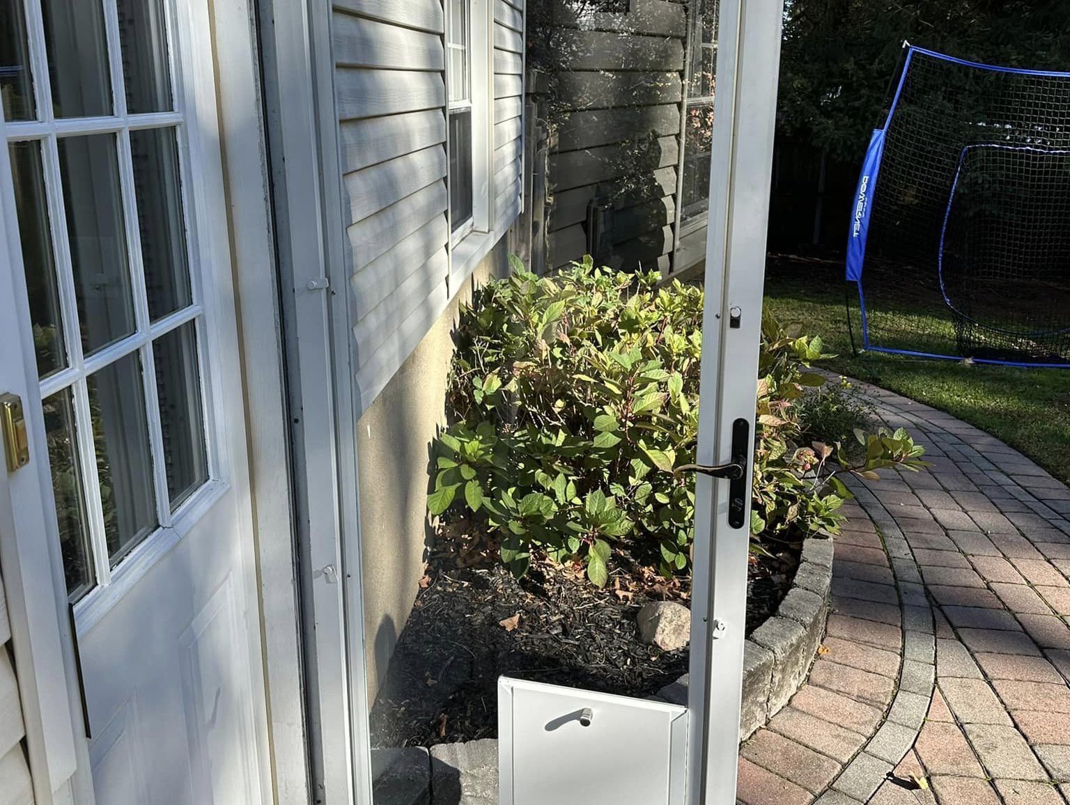 Side yard with white house siding, brick walkway, shrubs, and a small white utility box.