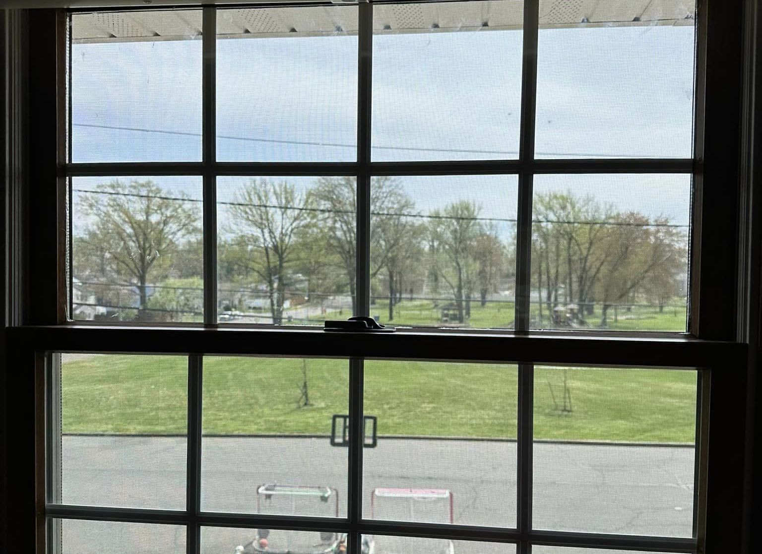 View through a window of a grassy field with trees and park benches outside
