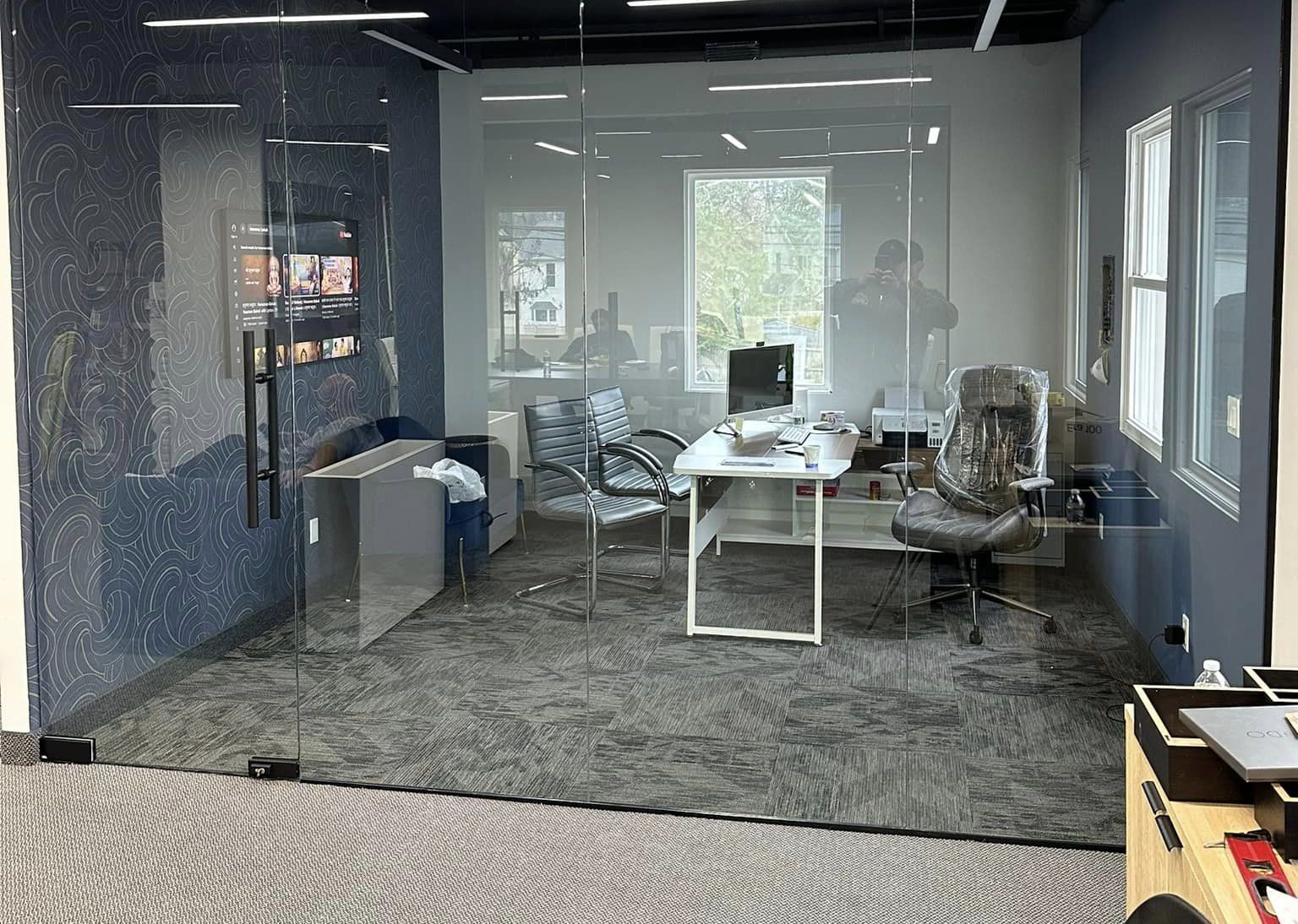 Modern office meeting room with glass walls, desk, chairs, and carpeted floor