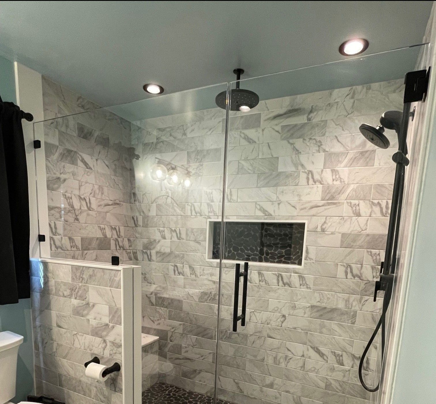 Modern tiled shower with glass door, black fixtures, and recessed ceiling lights.