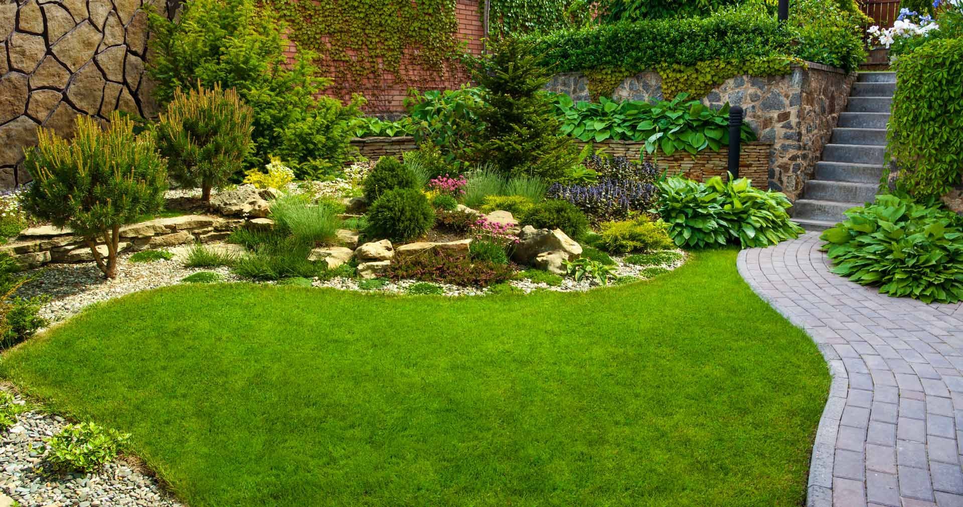 A lush green garden with a brick walkway and stairs leading up to it.