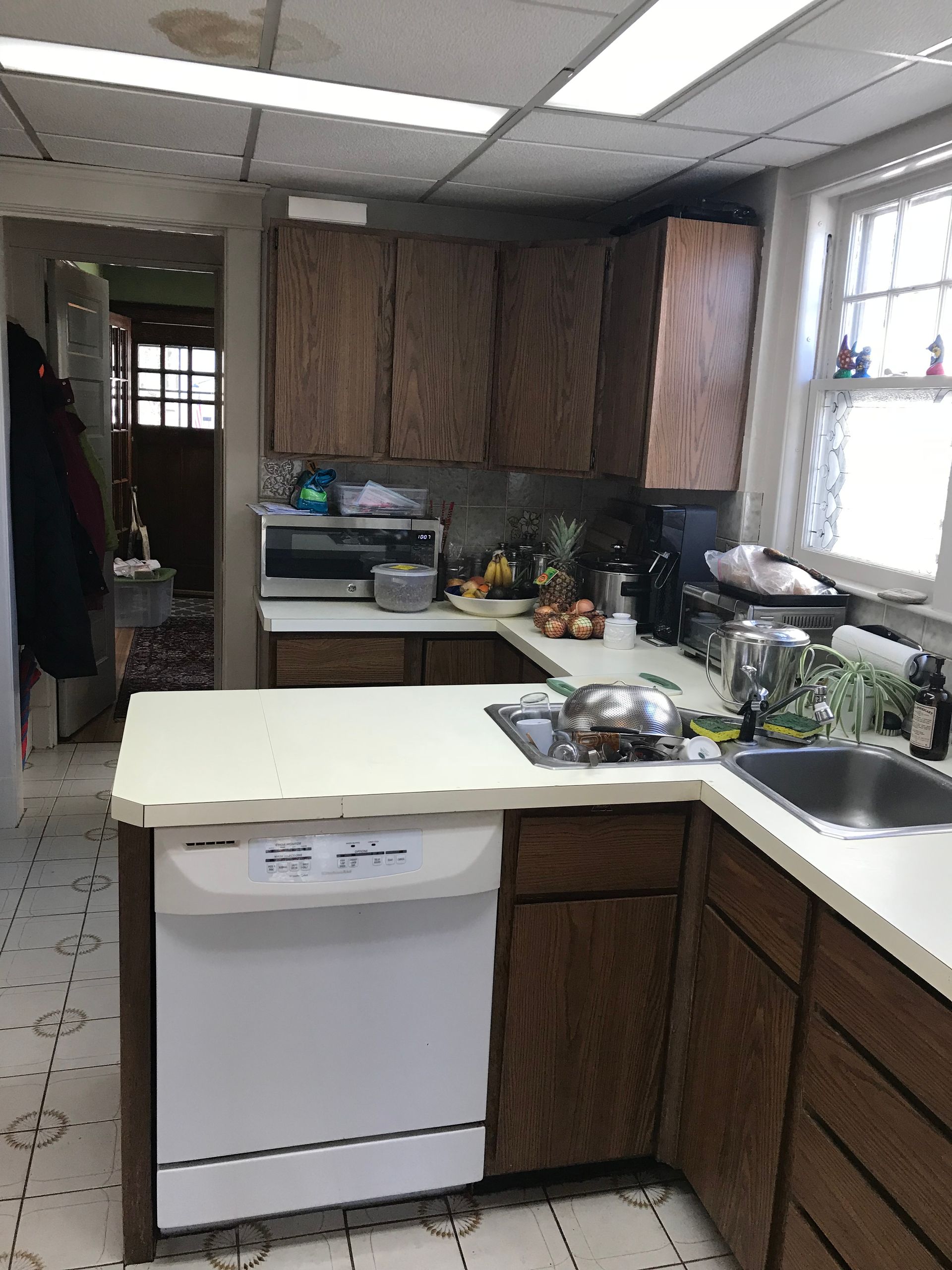 A kitchen with wooden cabinets , a white dishwasher , a sink , and a microwave.