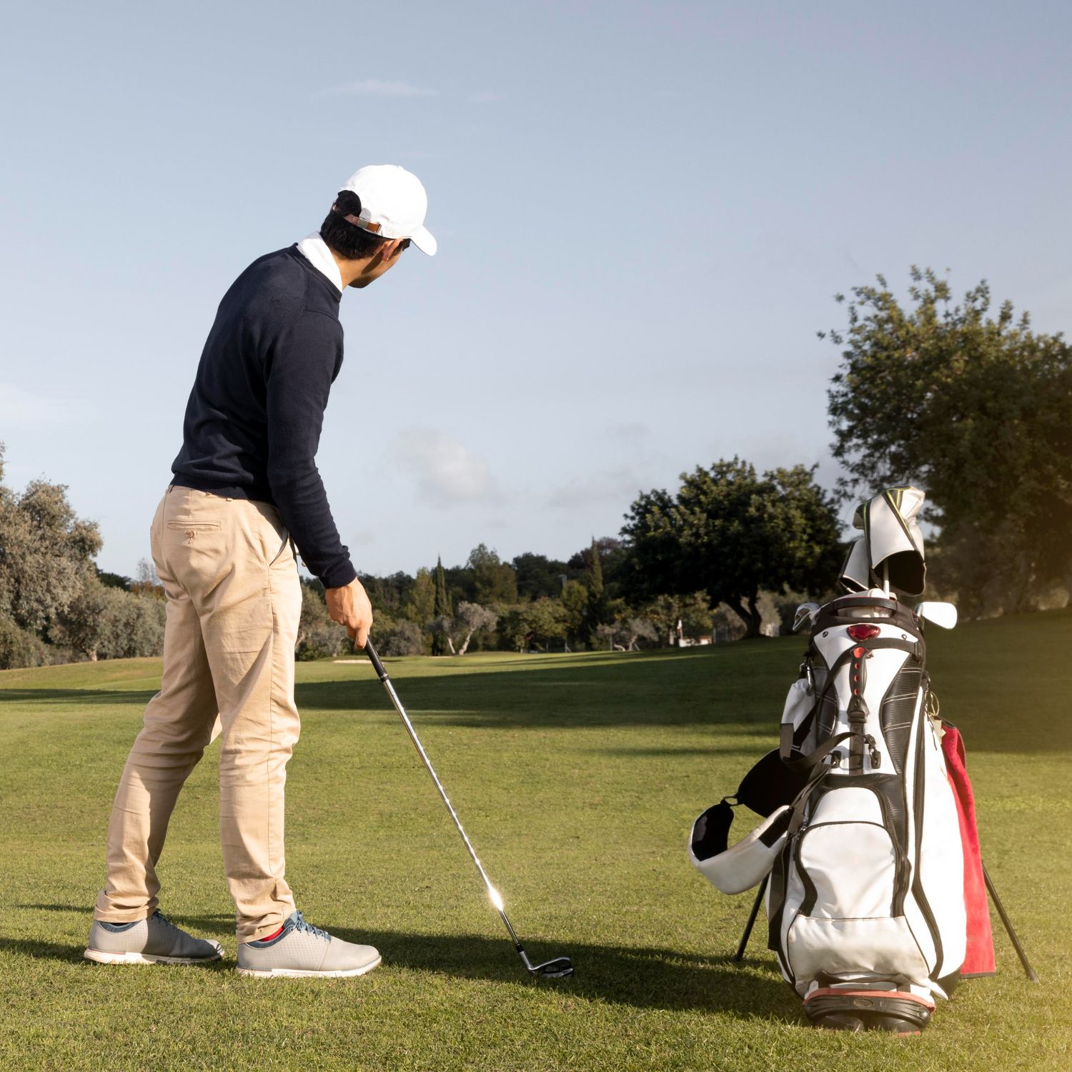 Golfer about to swing club on a sunny golf course, next to a golf bag.