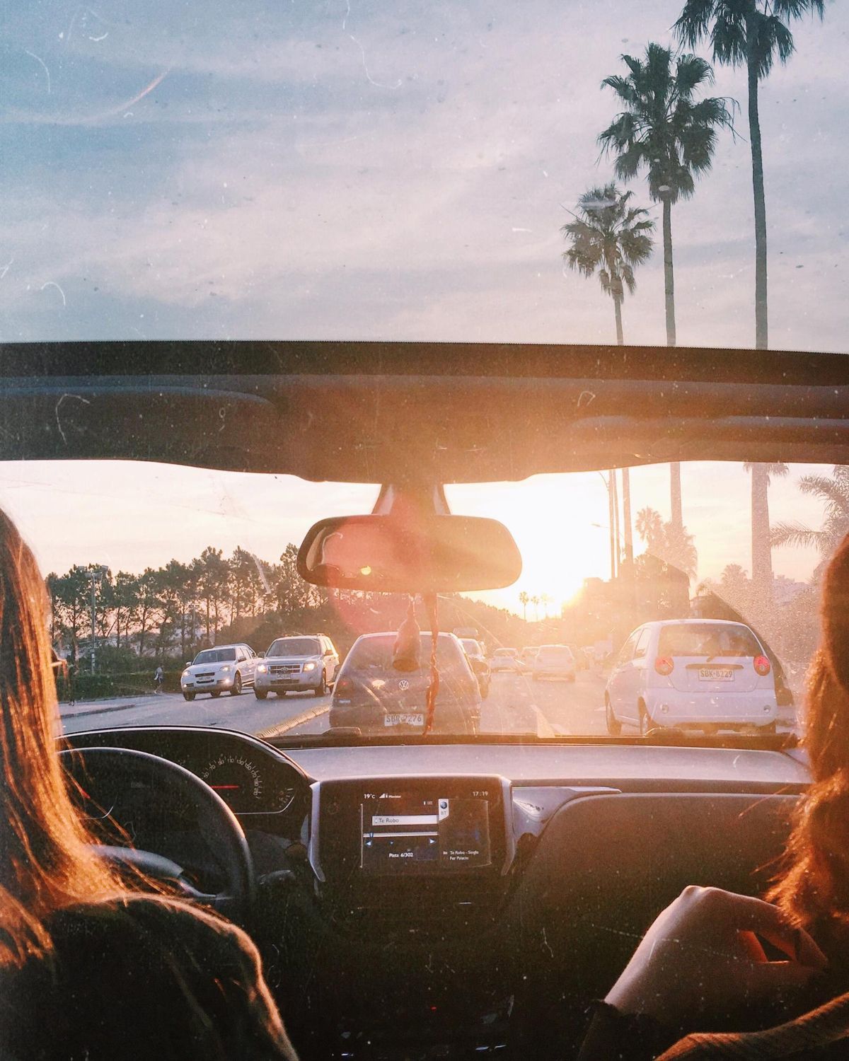 Car interior view. Two people driving towards sunset with palm trees, golden light.