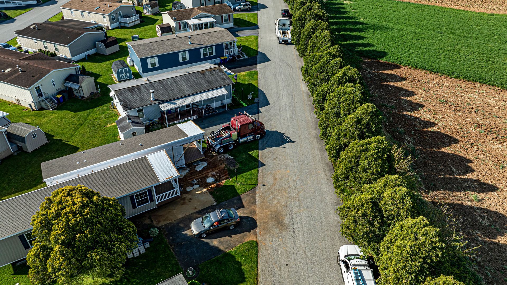 Aerial view: Mobile homes, road with shrubs, and farm fields. A truck is parked near the homes.