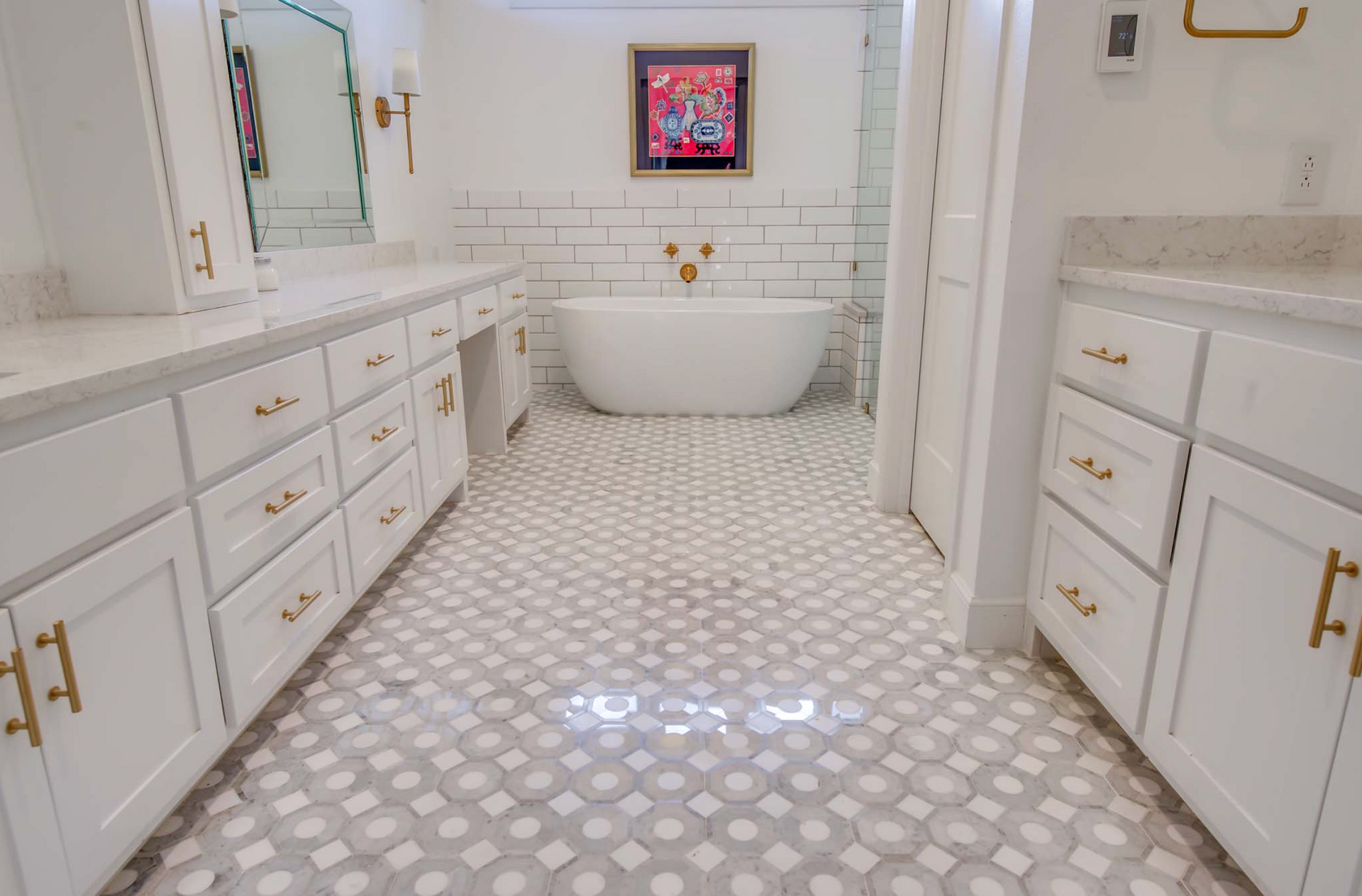 Bright white bathroom with a patterned floor, free-standing tub, and matching vanities with gold hardware.