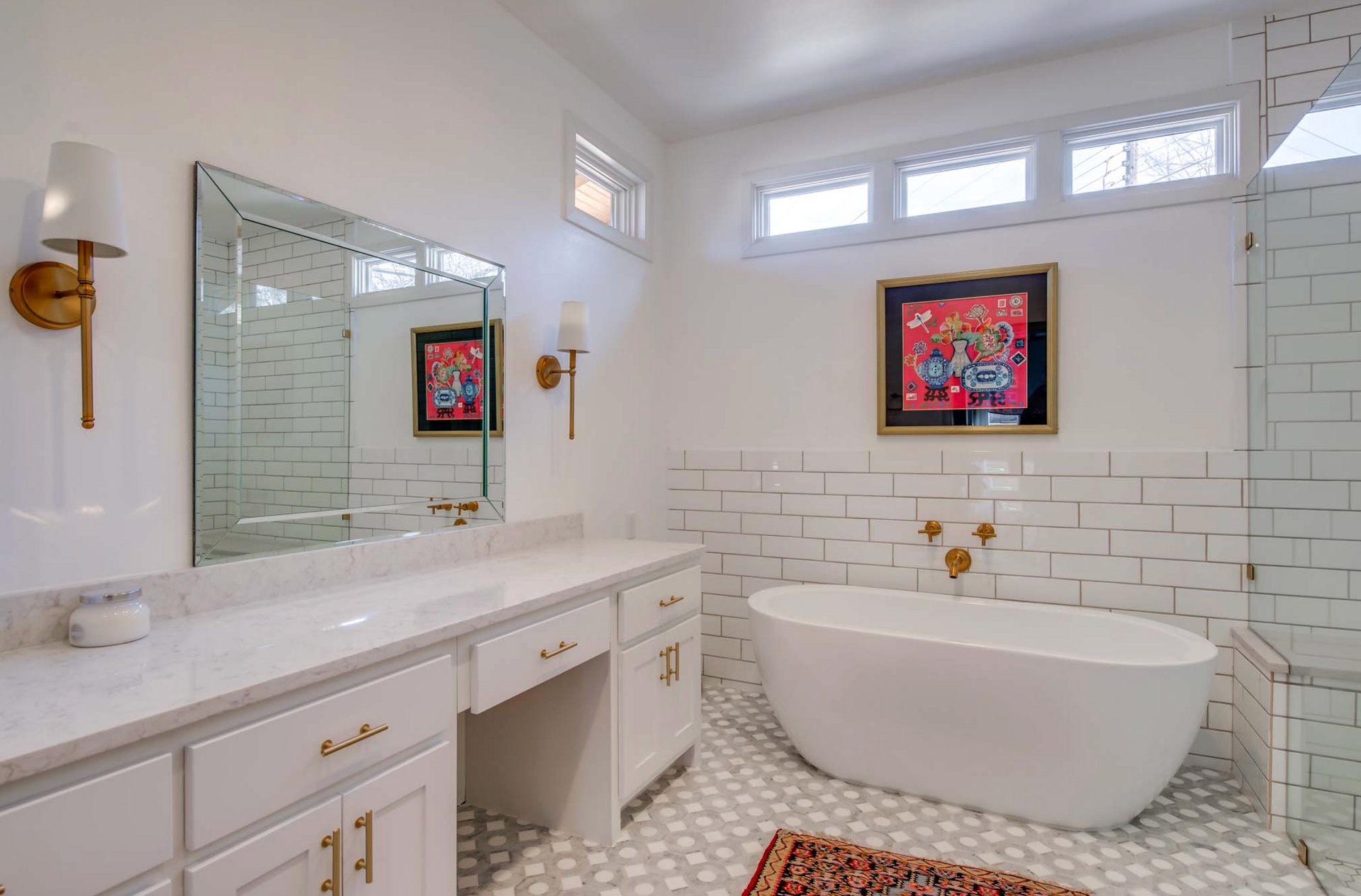 White bathroom with freestanding tub, vanity, and artwork on a tiled wall.