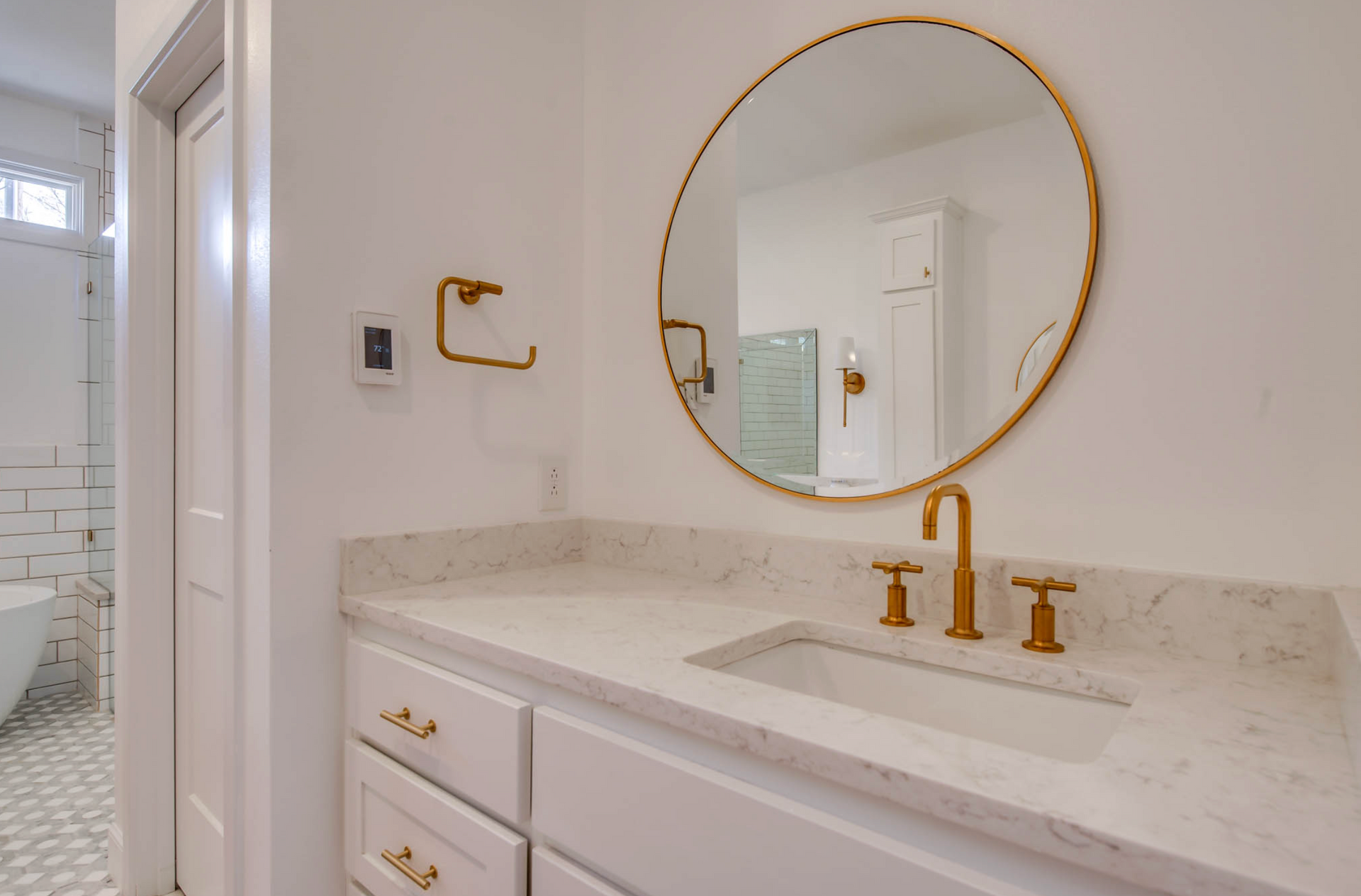 Bathroom with white countertop, gold fixtures, and round mirror.