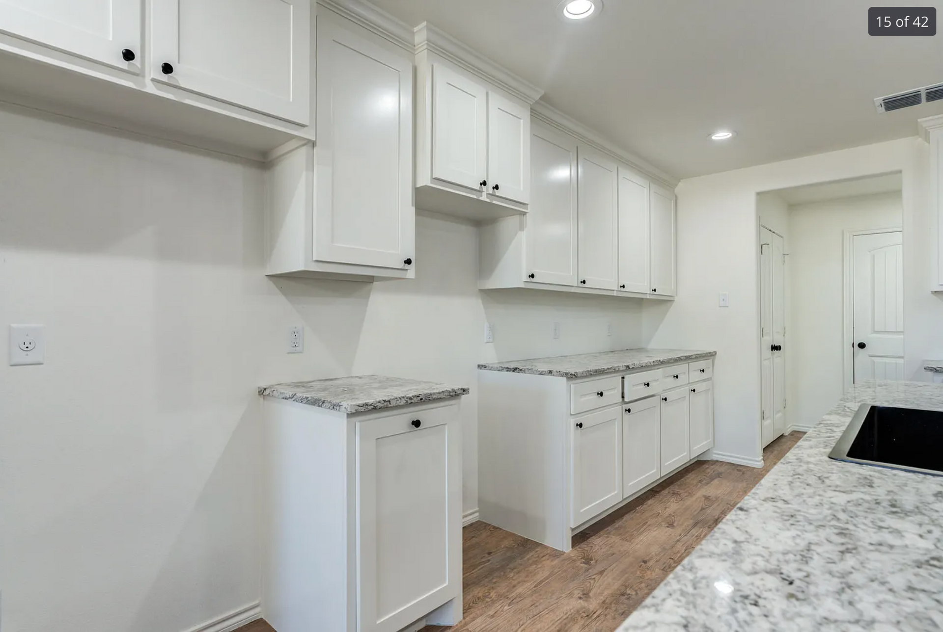 White kitchen with cabinets, granite countertops, and wooden floors.