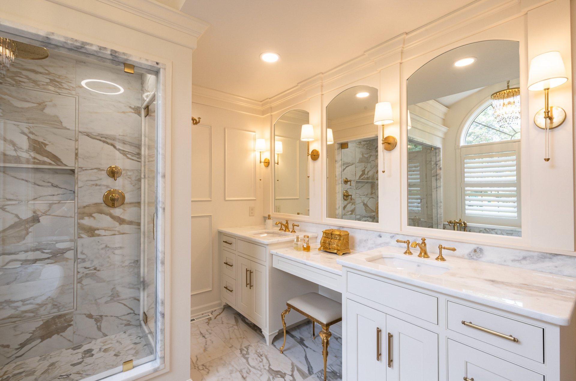Elegant white marble bathroom with double vanity, arched mirrors, and glass shower enclosure