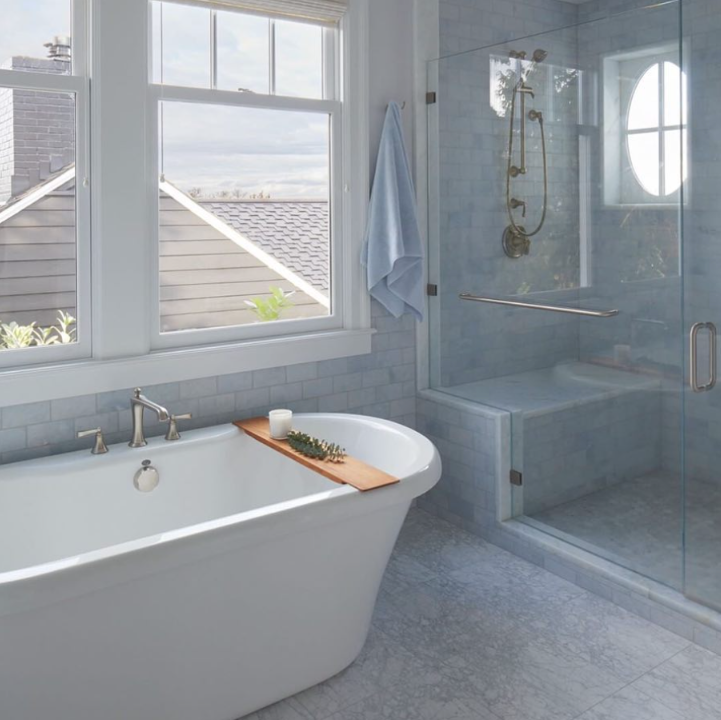 Modern bathroom with freestanding tub, walk-in glass shower, and large windows with ocean view.