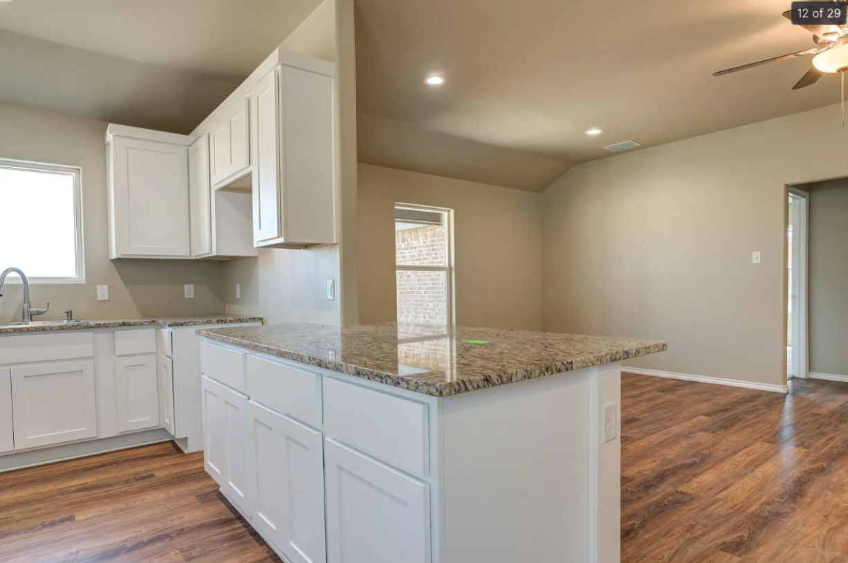 Bright kitchen with white cabinets, granite island, and wood floors opening to an adjacent living area