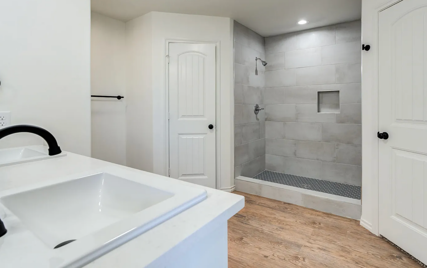 Bright modern bathroom with white vanity, walk-in tiled shower, and wood-look flooring