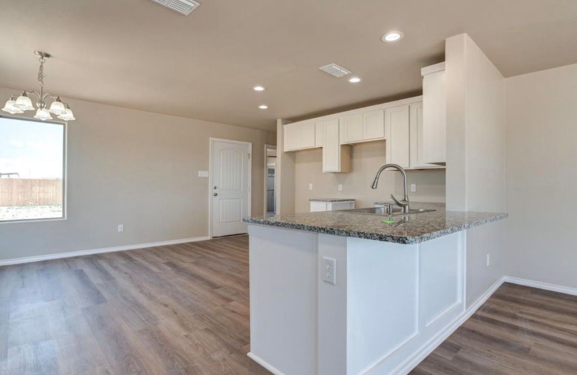 Empty modern kitchen and living area with granite island, white cabinets, and wood-look flooring