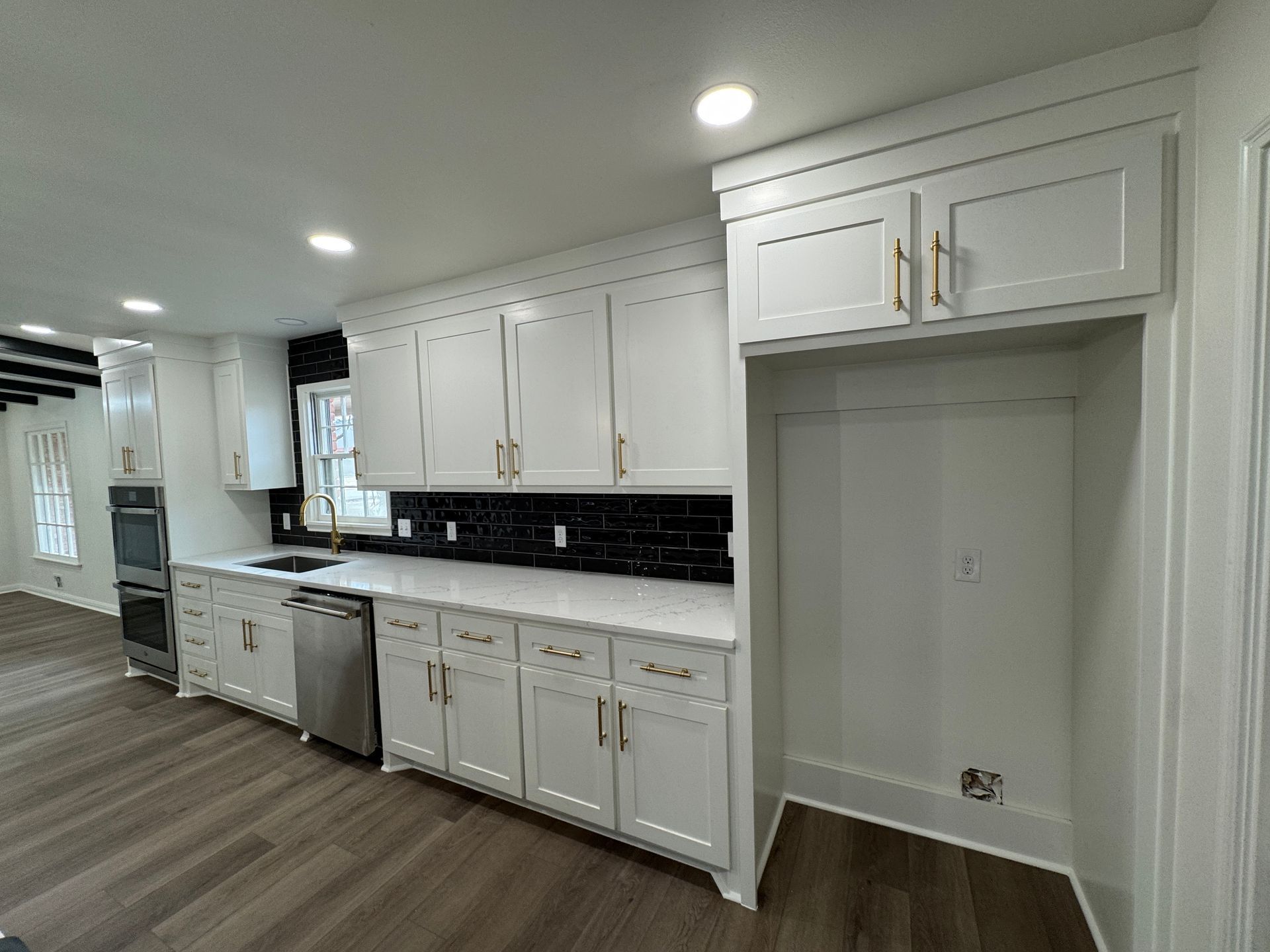 White kitchen with upper and lower cabinets, black backsplash, built-in refrigerator, and stainless steel appliances.
