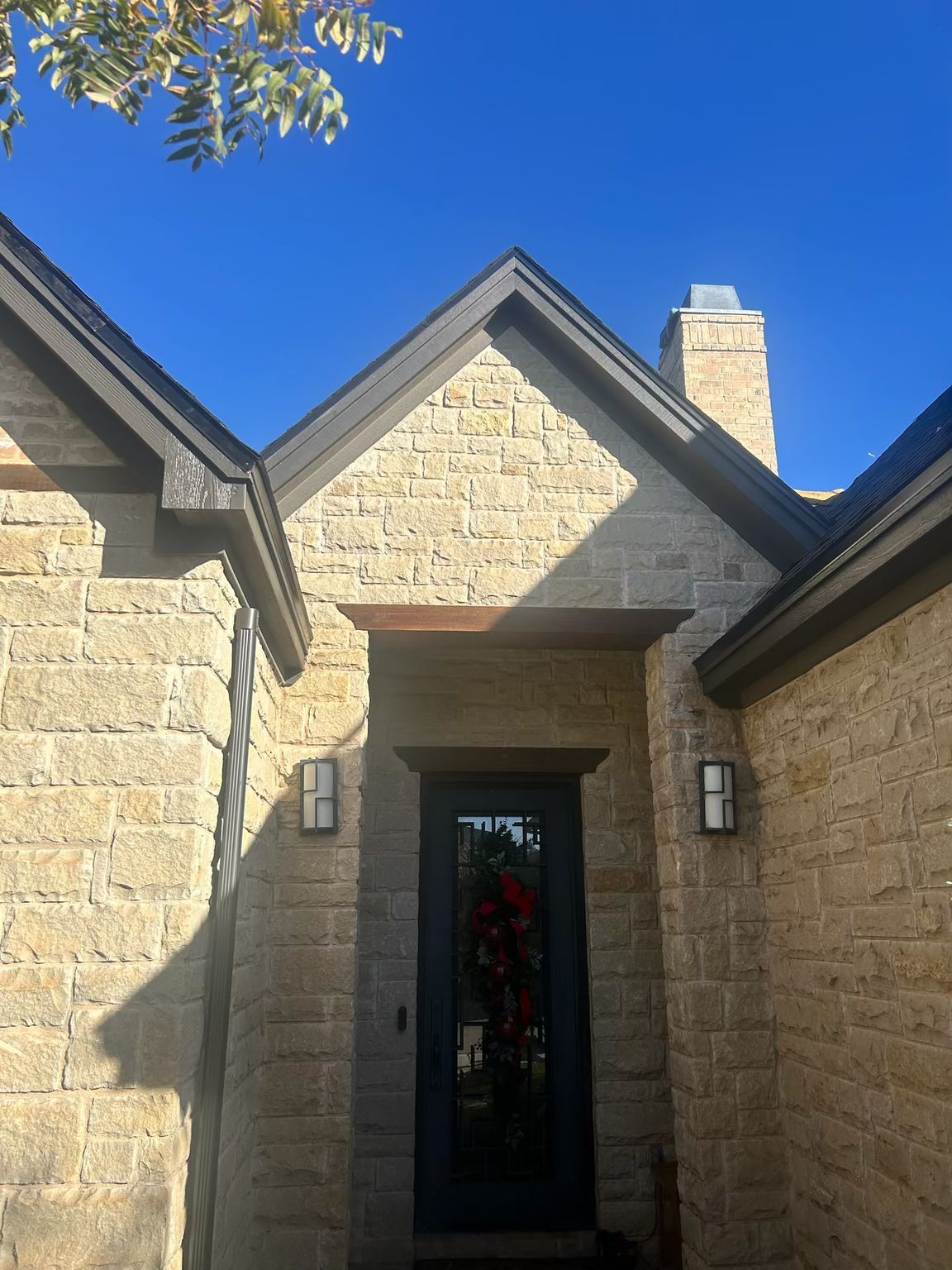 Tan stone house exterior with dark trim and front door, blue sky.