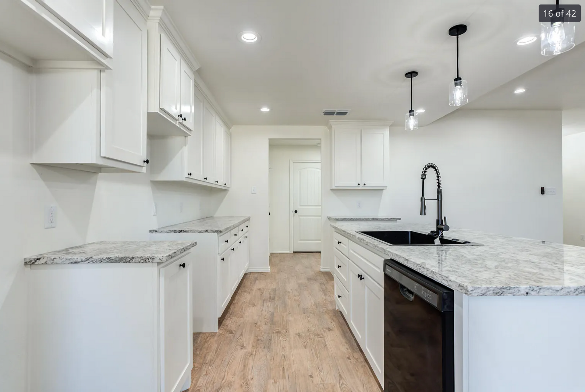 Bright white modern kitchen with marble countertops, island sink, pendant lights, and wood flooring