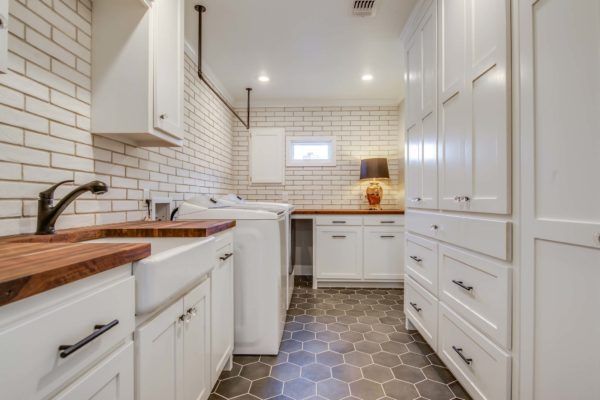 Laundry room with white cabinets, brick backsplash, wood countertops, and hexagonal tile floor.