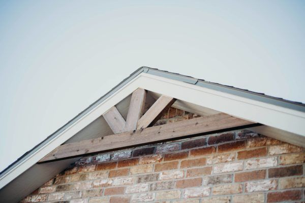 Brick home gable with wooden decorative beams under the roof's edge, against a pale sky.