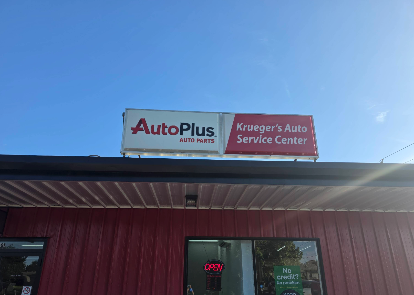 AutoPlus and Krueger's Auto Service Center signs on a red auto shop under a blue sky | Krueger's Auto Service Center
