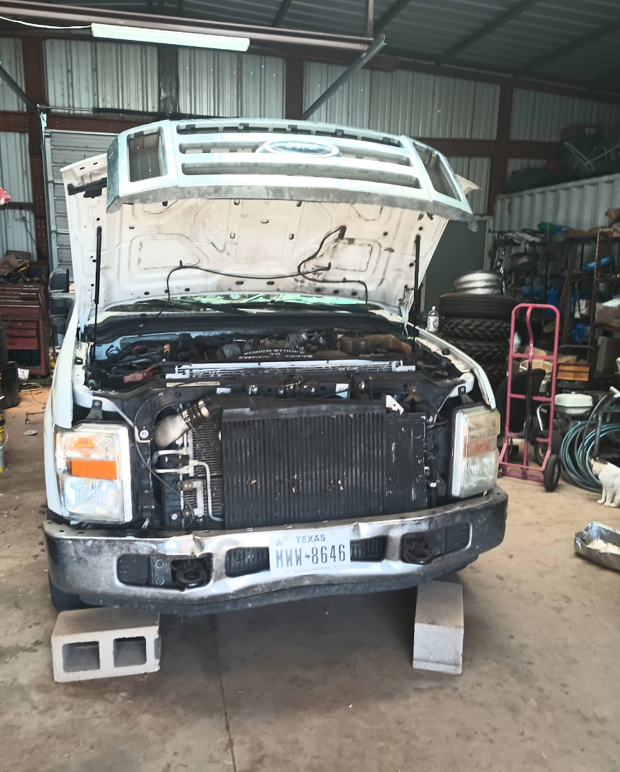 White truck with hood open in a workshop, showing the engine and front damage. | Krueger's Auto Service Center