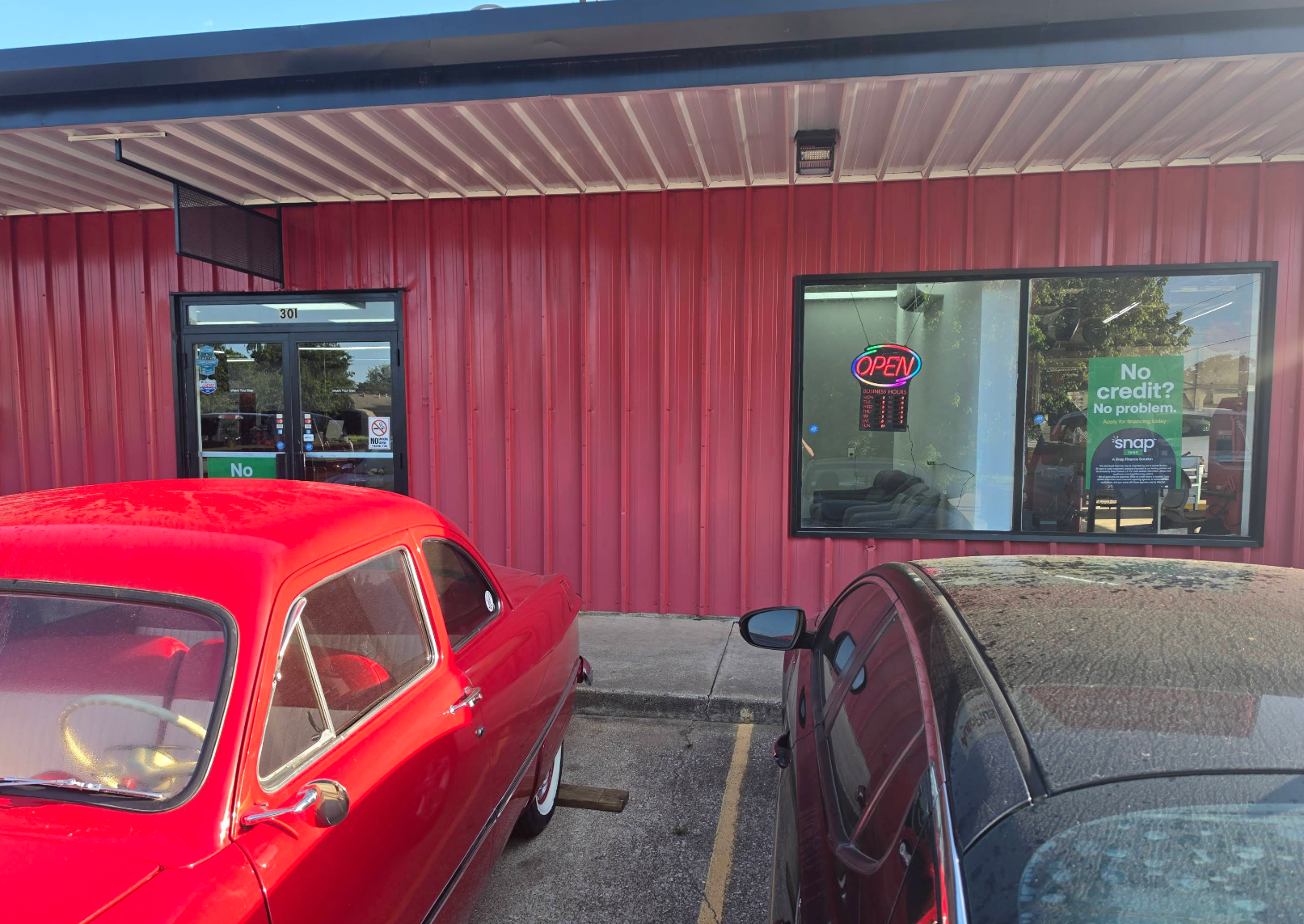 Red storefront with glass door and window, parked red and black cars in front. | Krueger's Auto Service Center