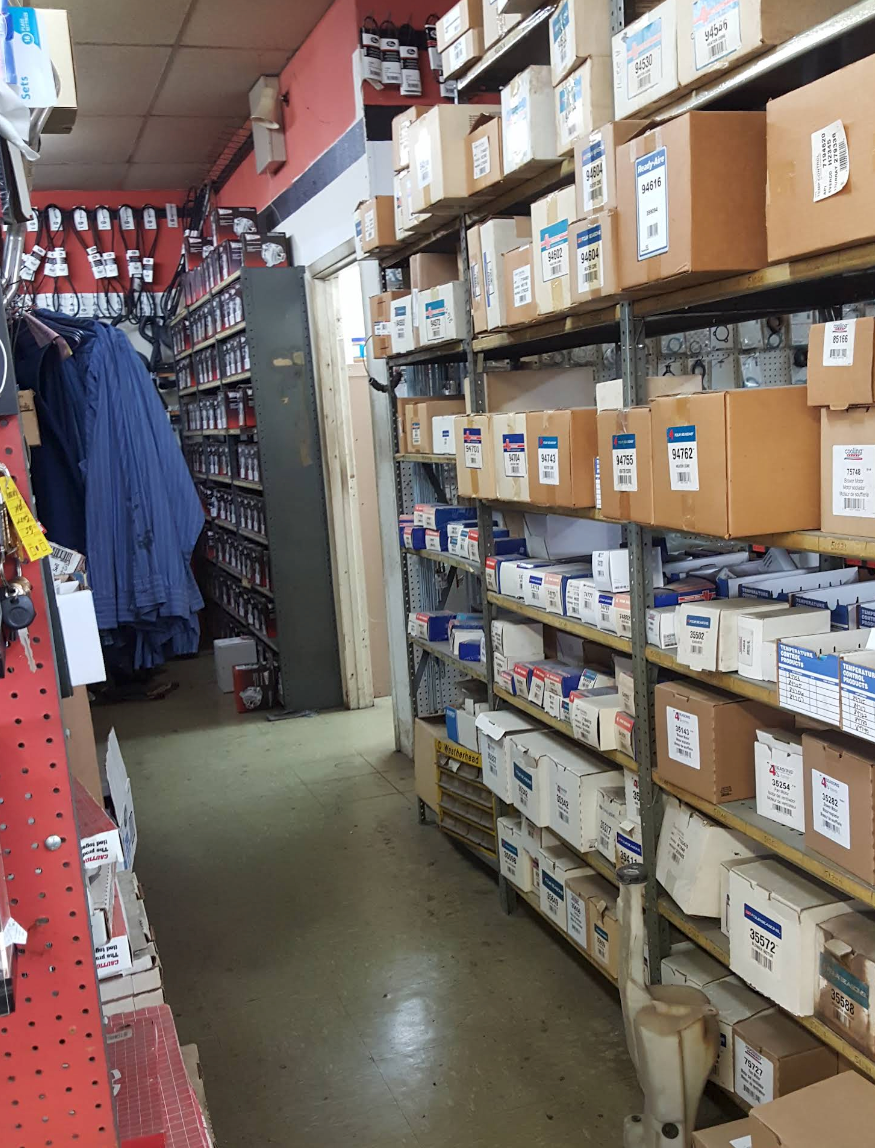 A narrow store aisle lined with shelves of labeled boxes and hanging coats. | Krueger's Auto Service Center