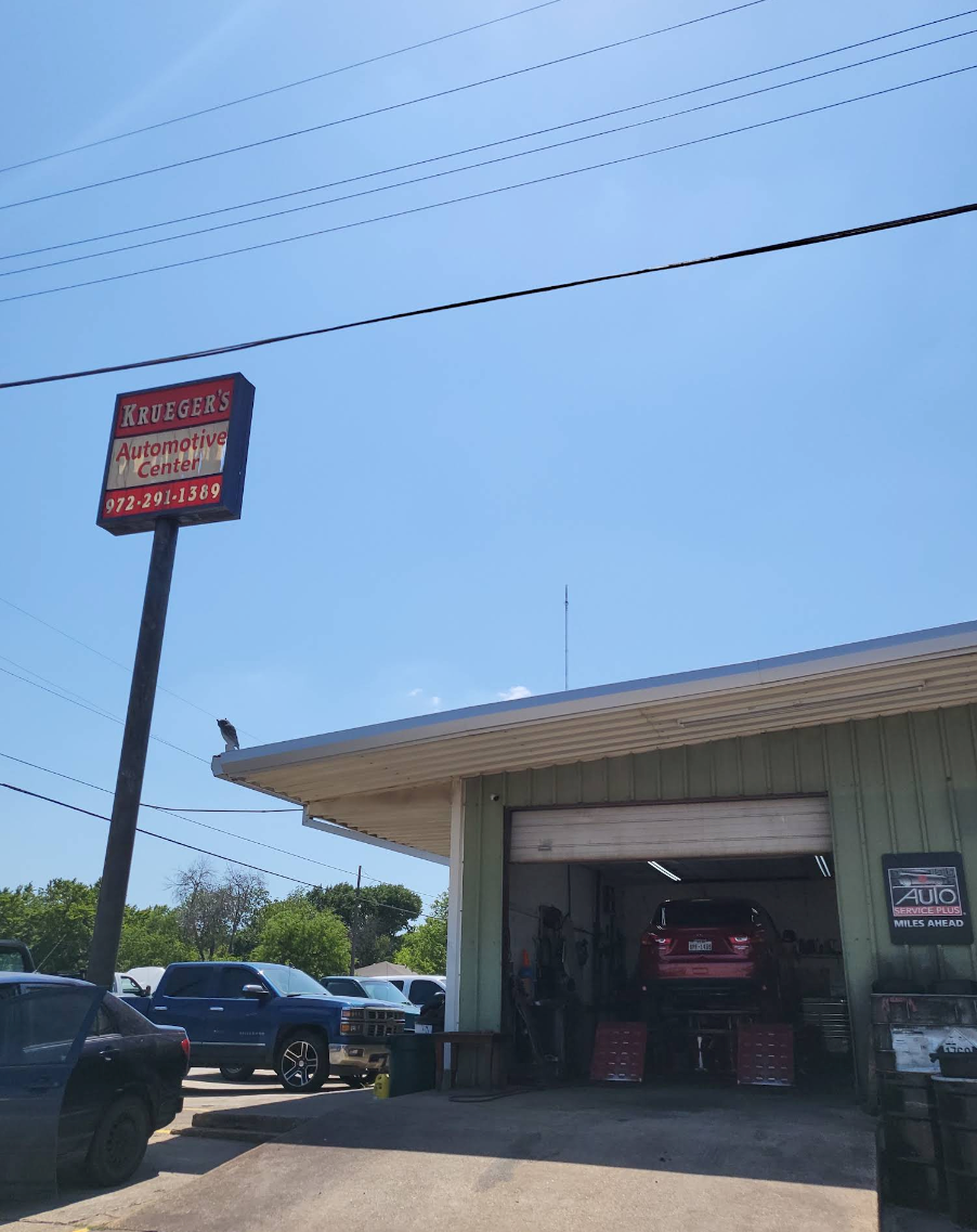 Auto repair shop exterior with a red sign, open garage bay, and parked vehicles under a clear blue sky | Krueger's Auto Service Center