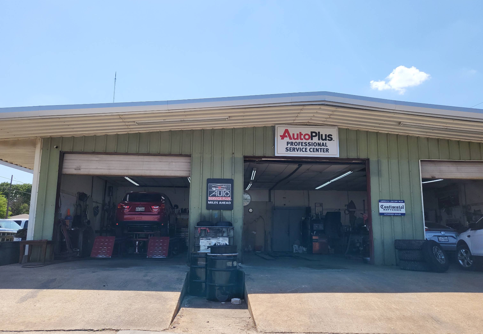 Auto repair garage with open bays and an Auto Plus sign under a clear blue sky | Krueger's Auto Service Center