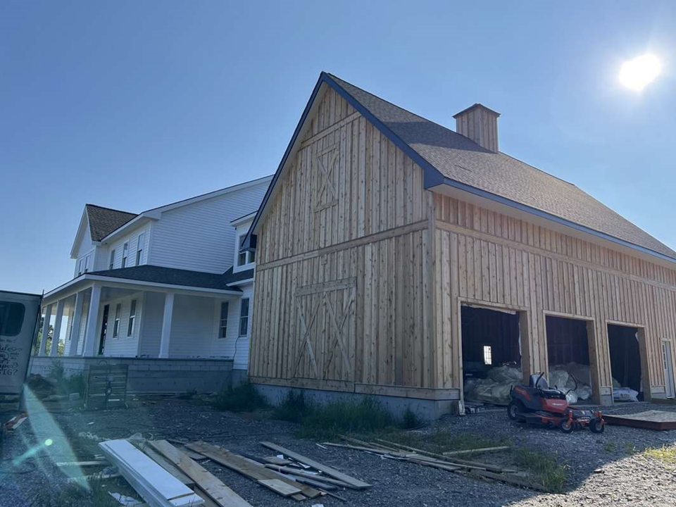 A large wooden barn is being built next to a house.