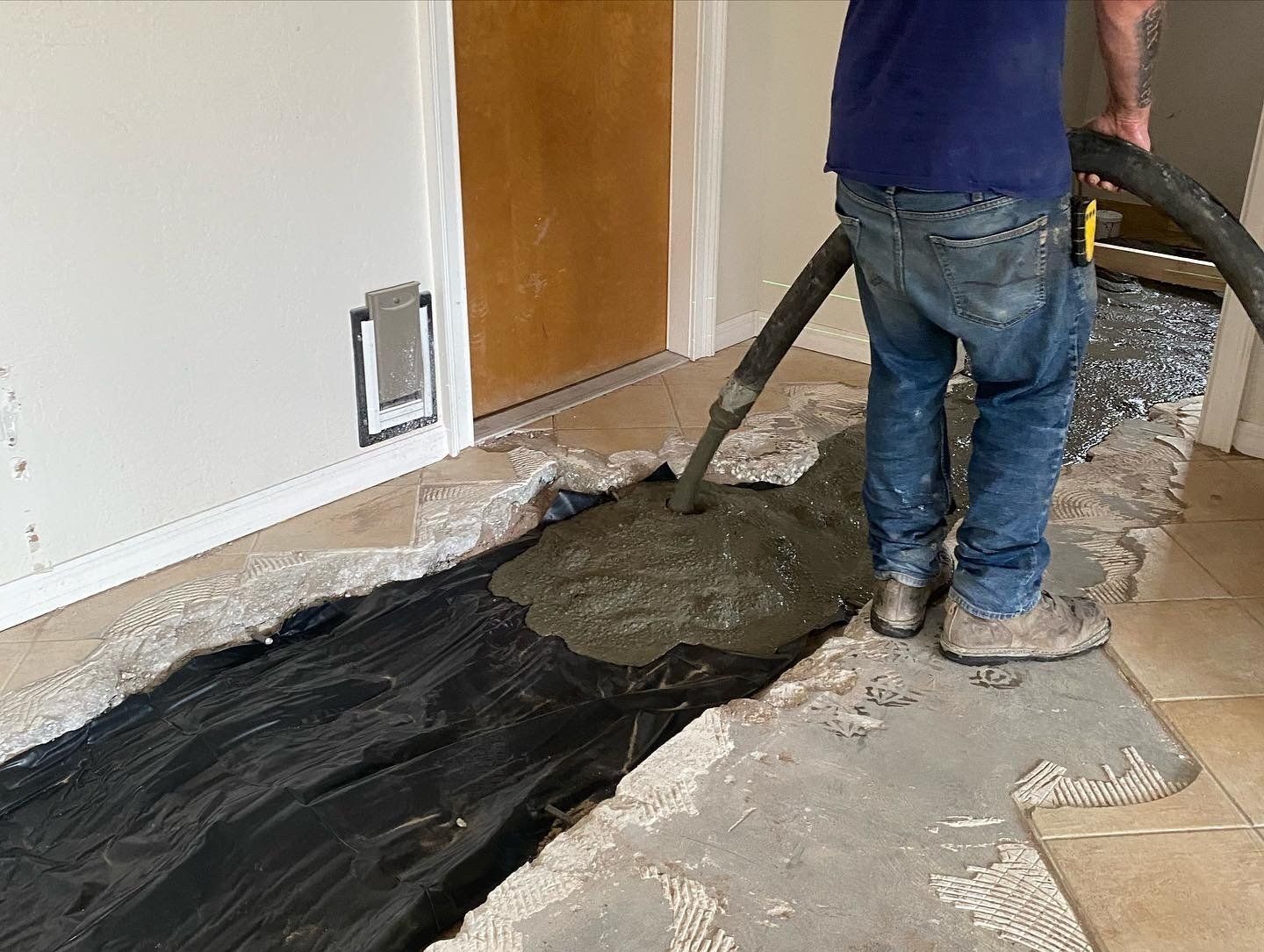 Worker pouring concrete over black plastic in a room under renovation