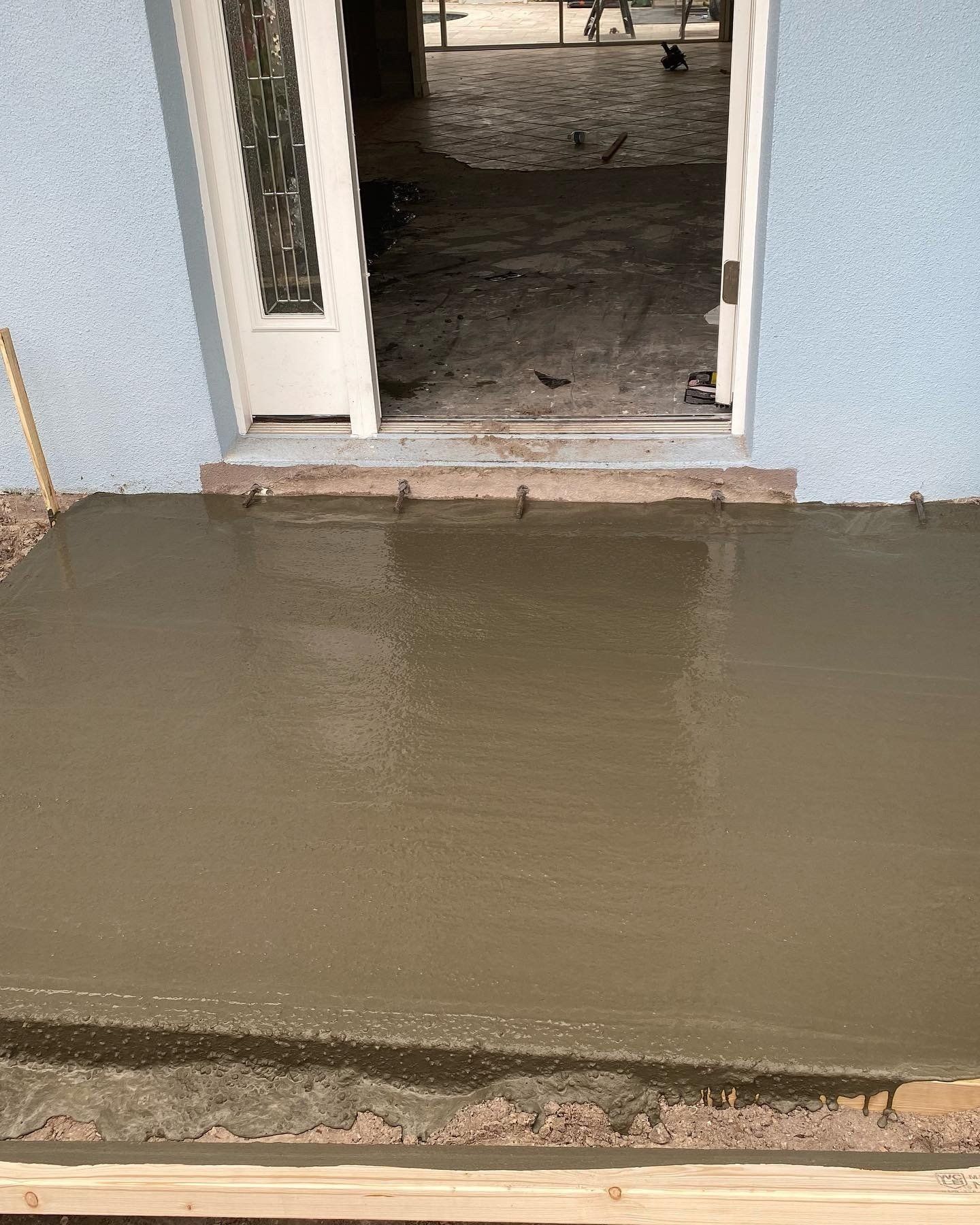 Fresh concrete slab poured at a doorway with a wet floor beyond it