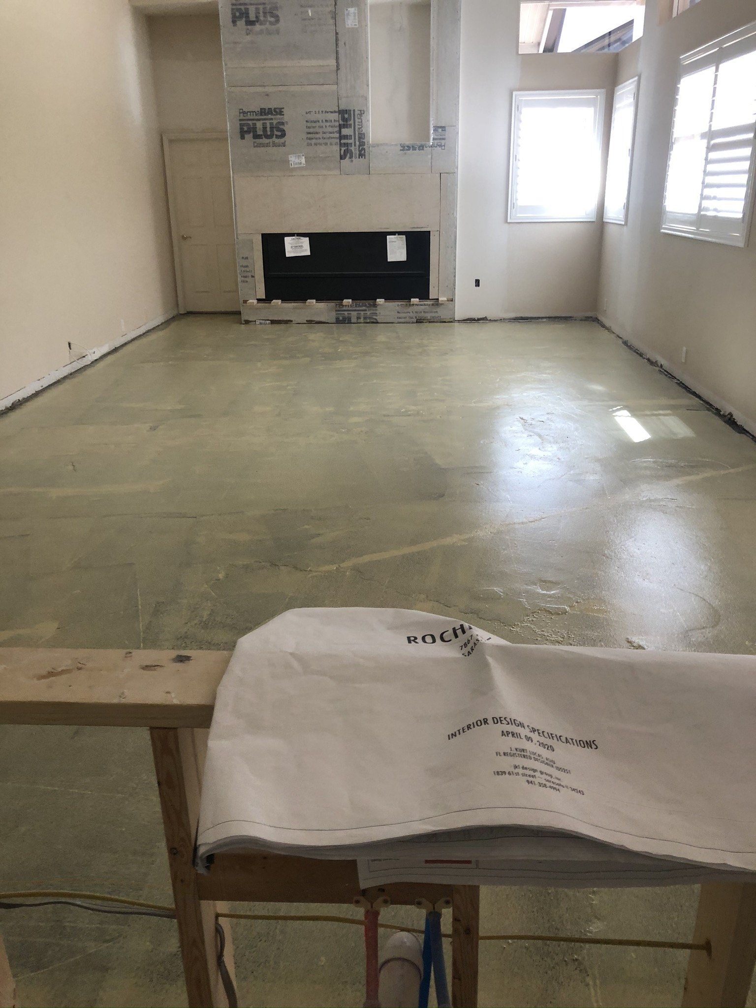 Empty room with concrete floor, windows on the right, and a wooden bench with a paper sheet in the foreground