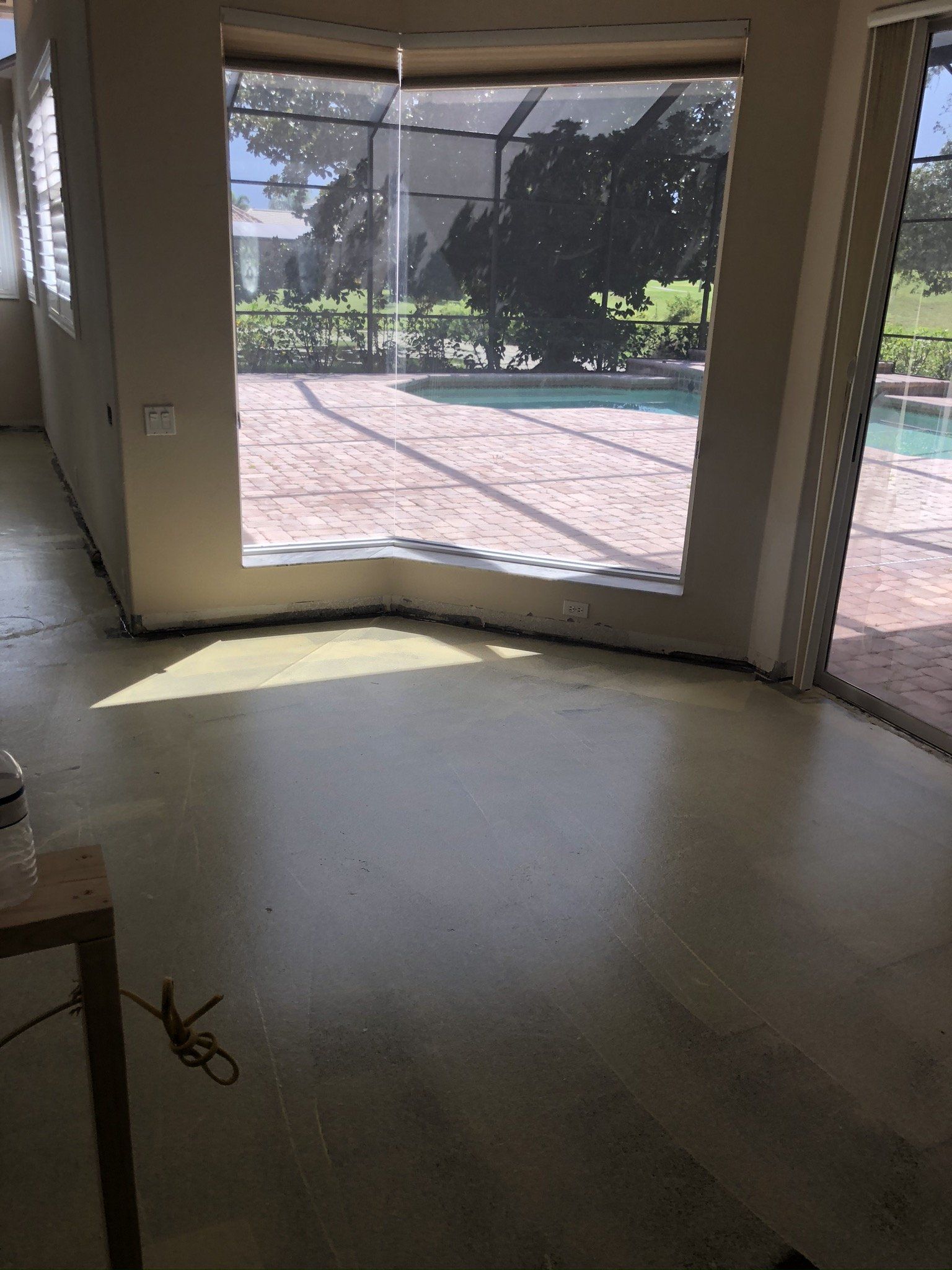 Empty living room with a large bay window overlooking a sunny patio and garden.