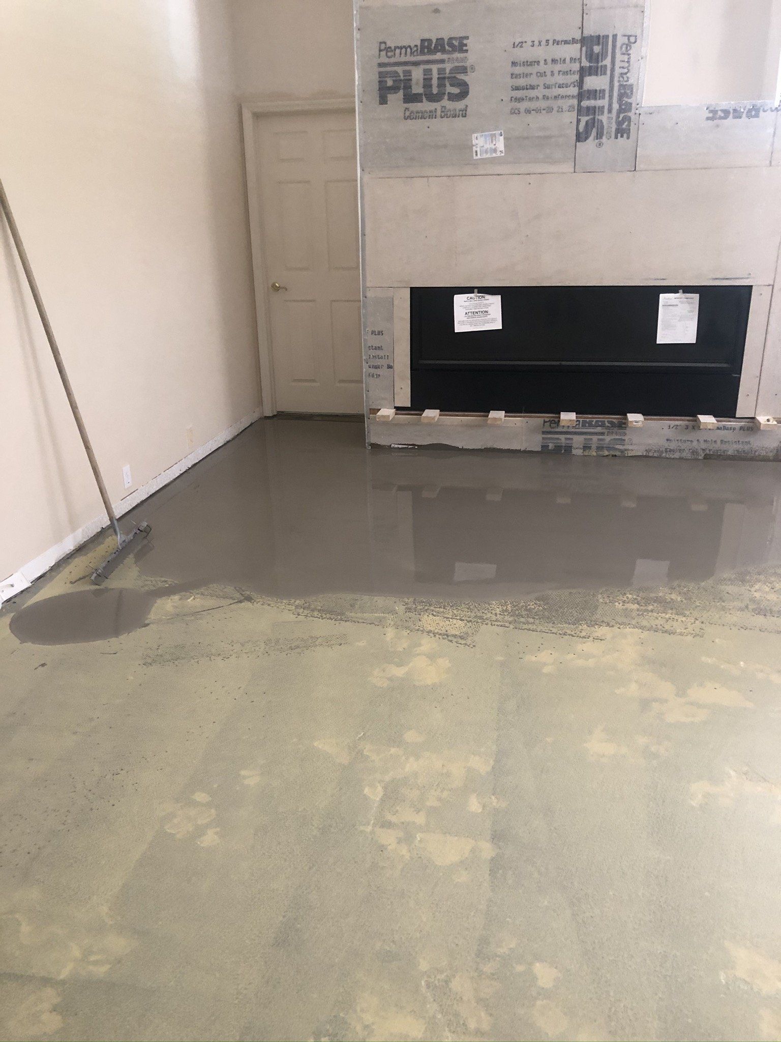 Empty room with wet concrete floor and a partially wrapped appliance or cabinet against the wall.