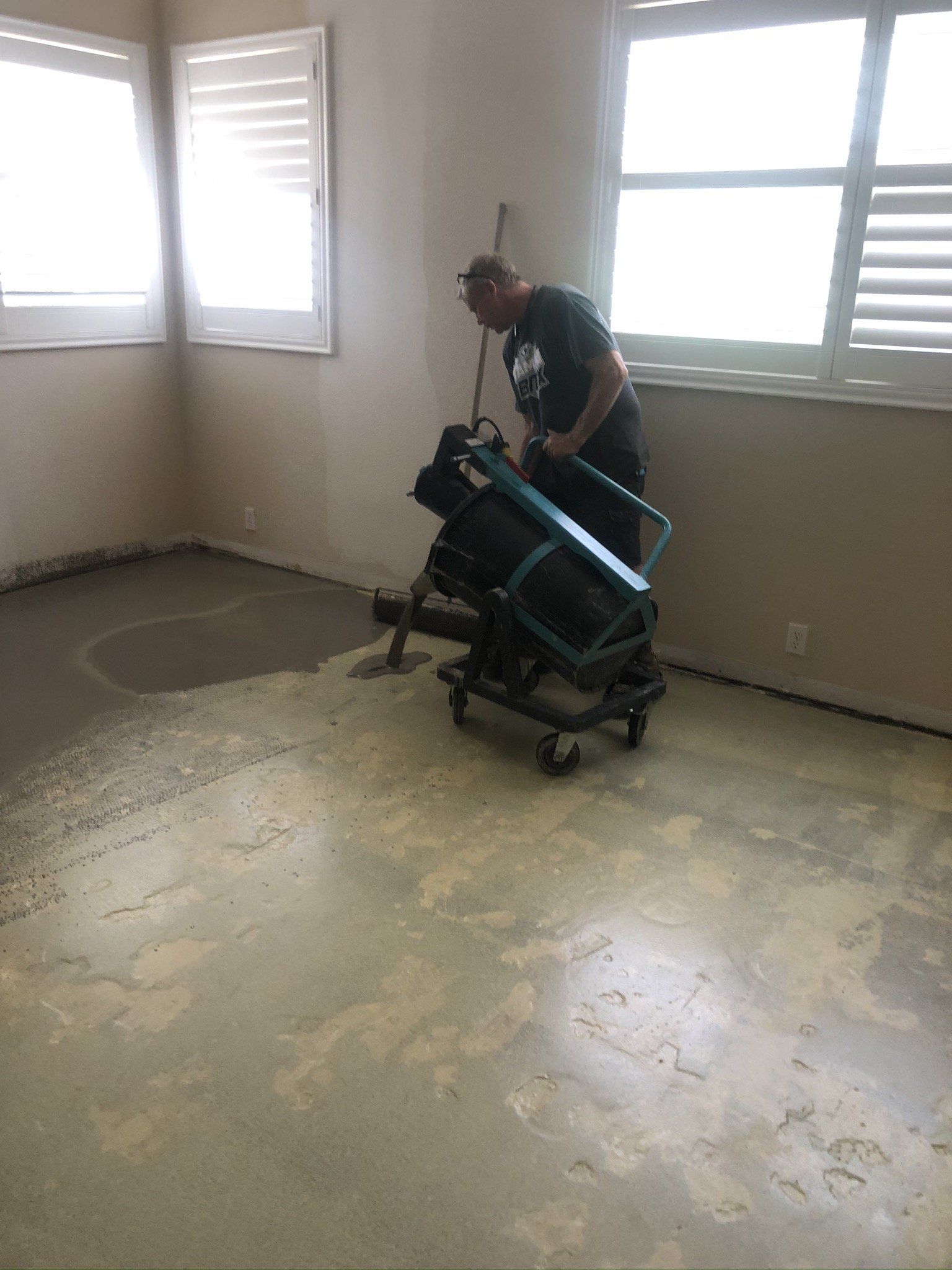 Person operating a floor grinder in a bare room with windows and a concrete floor