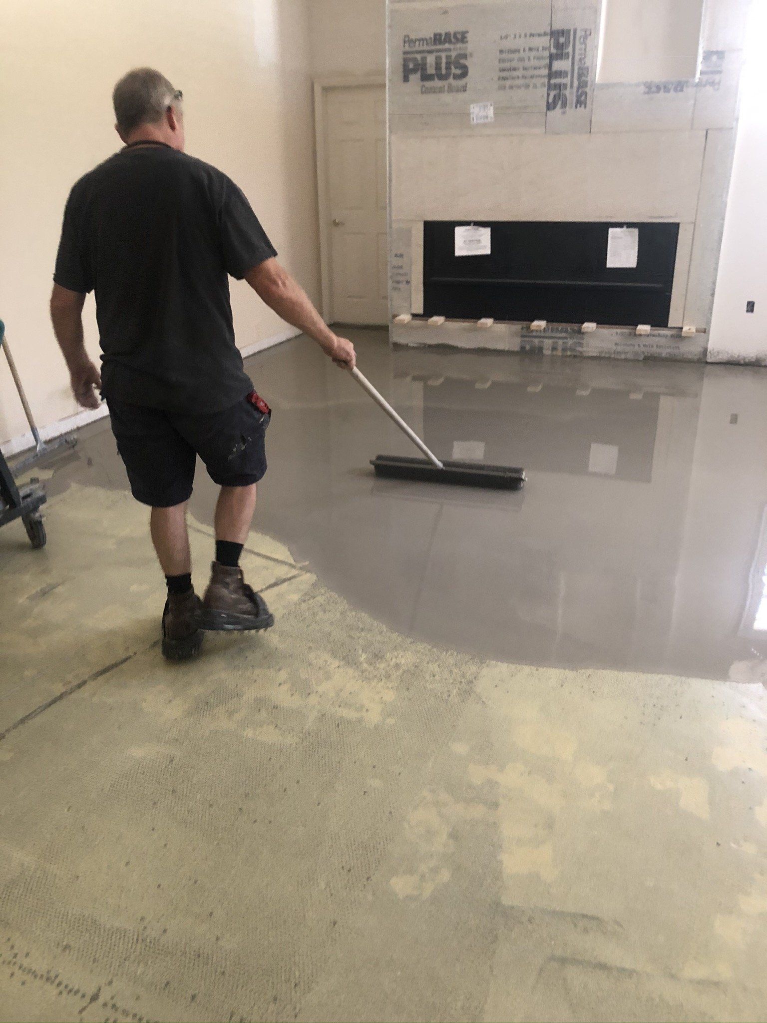 Worker spreading gray floor coating with a squeegee in a garage-like room